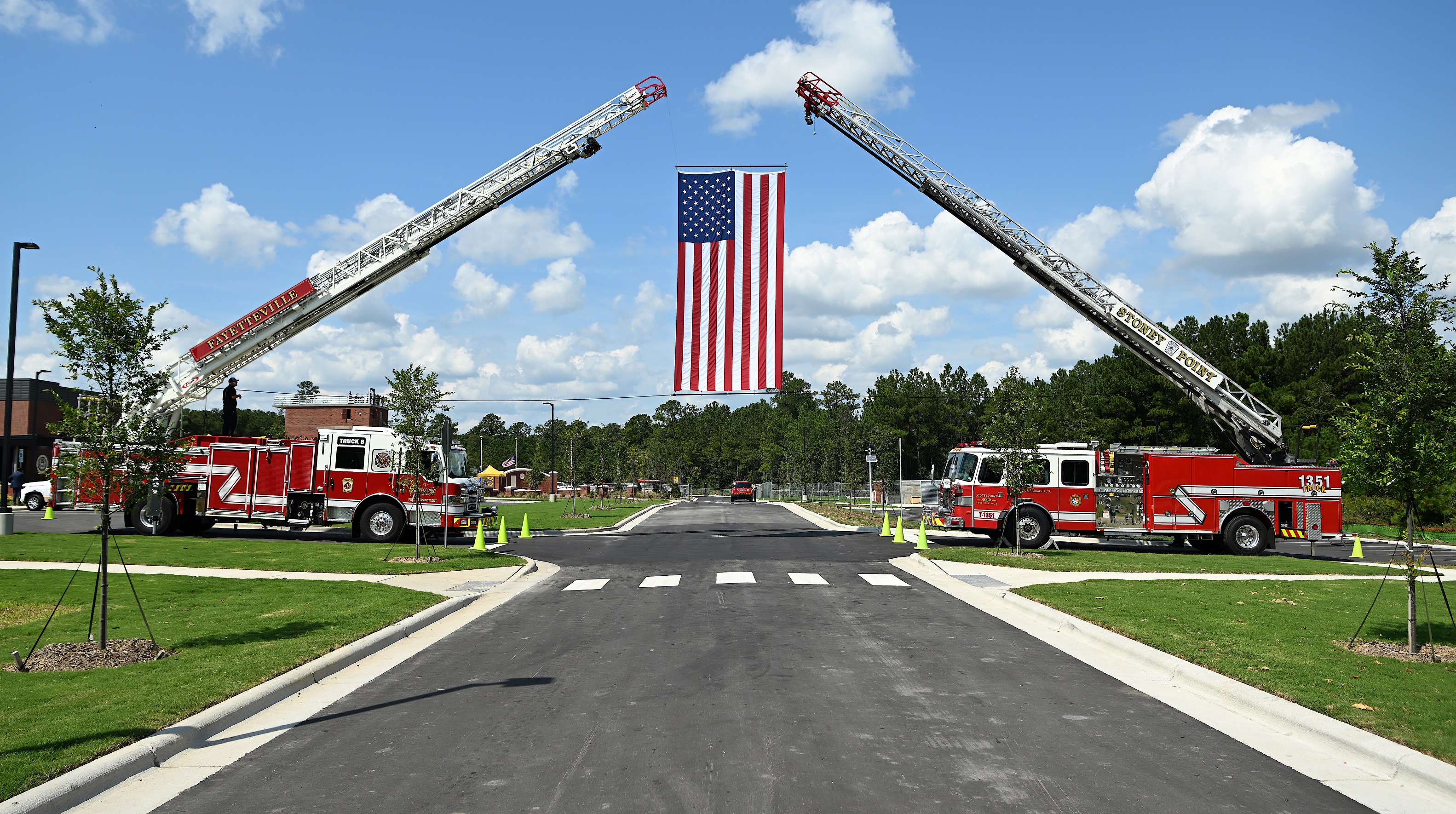 A United States flag hangs between two fire truck ladders extended off of trucks.