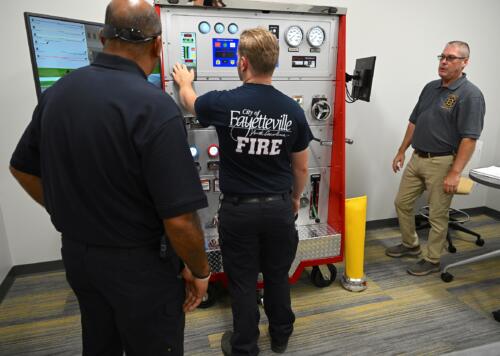 Three men look at an instrument panel in a simulation lab.