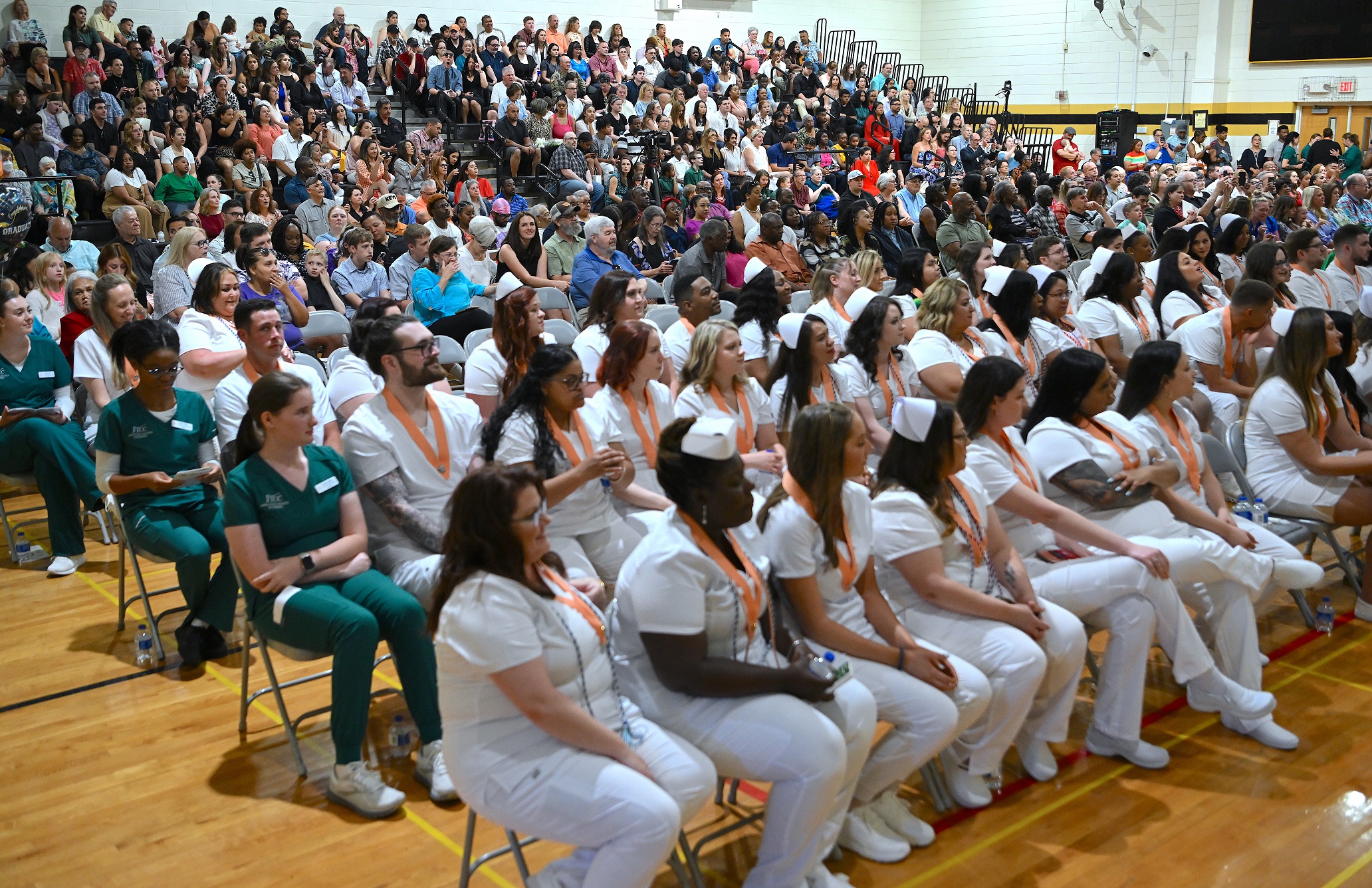 Rows of graduates in white nurse uniforms sit in front of a full audience in the Horace Sisk Building.