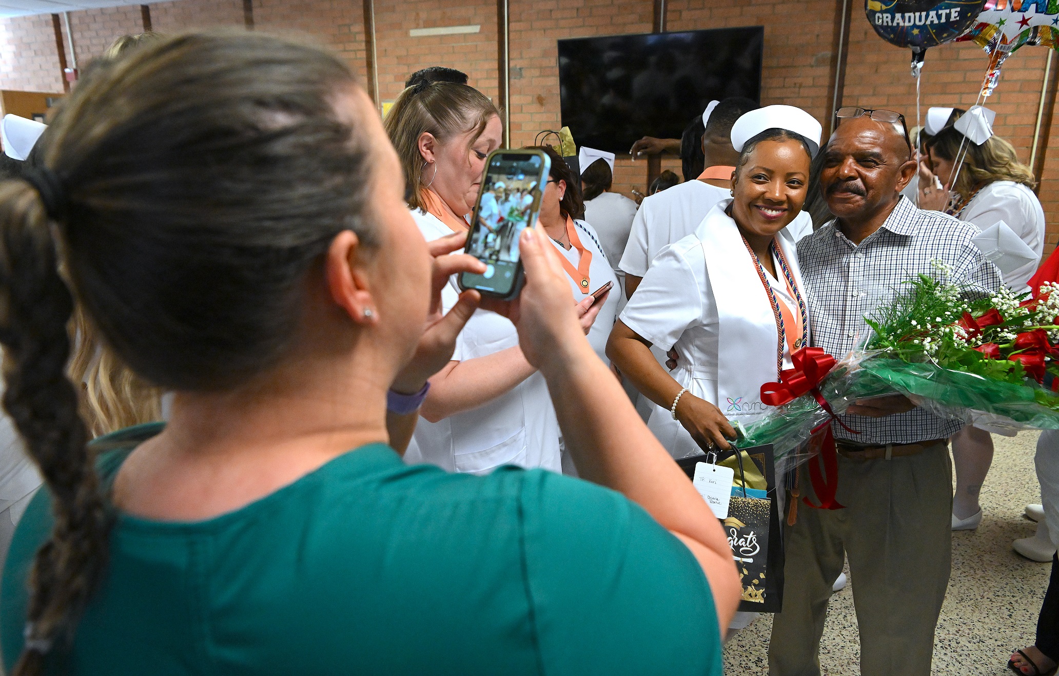 A photo of a woman taking a photo of a Nursing graduate and a loved one.