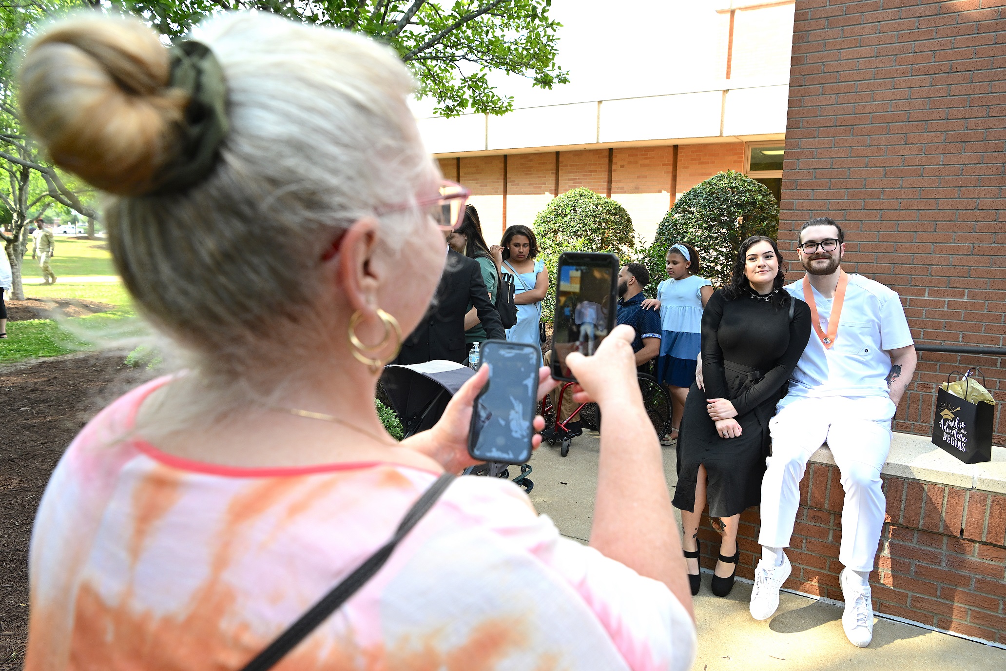 A photo of a woman taking a photo of a Nursing graduate and a loved one.