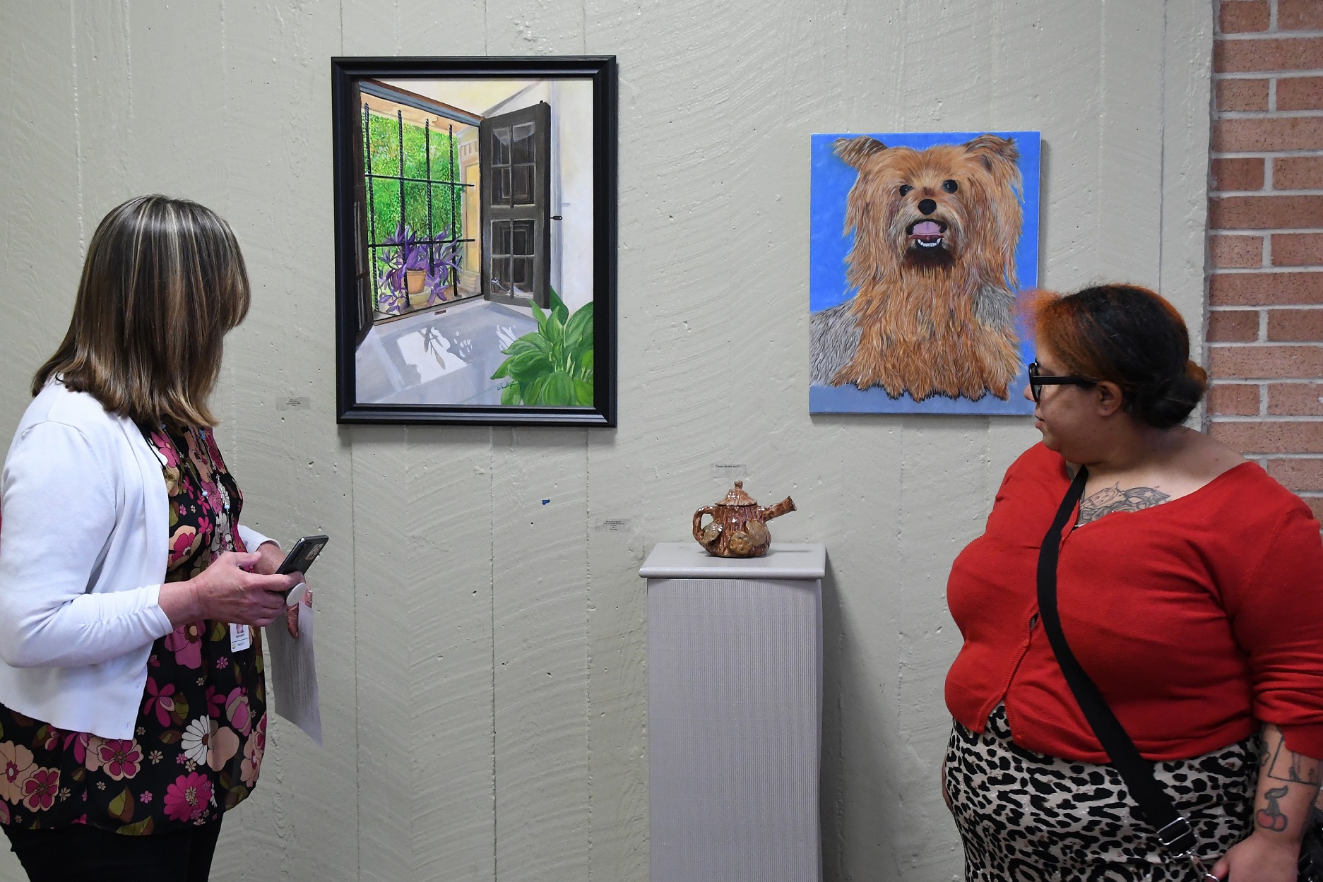 Two women look at paintings and a piece of pottery during the art exhibition opening reception.