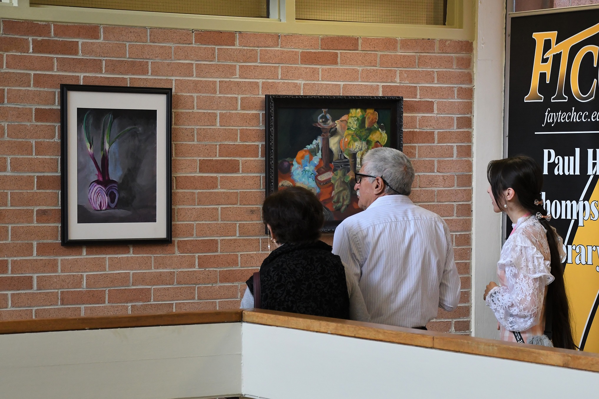Three visitors look at a piece of art hanging on the wall inside the library.