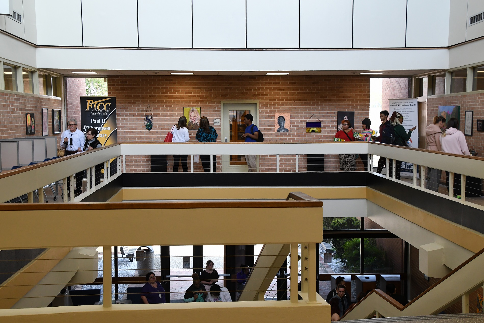 A wide photo of the second floor walkway inside the Paul H. Thompson Library. Visitors look at the artwork hanging on the walls around the walkway.