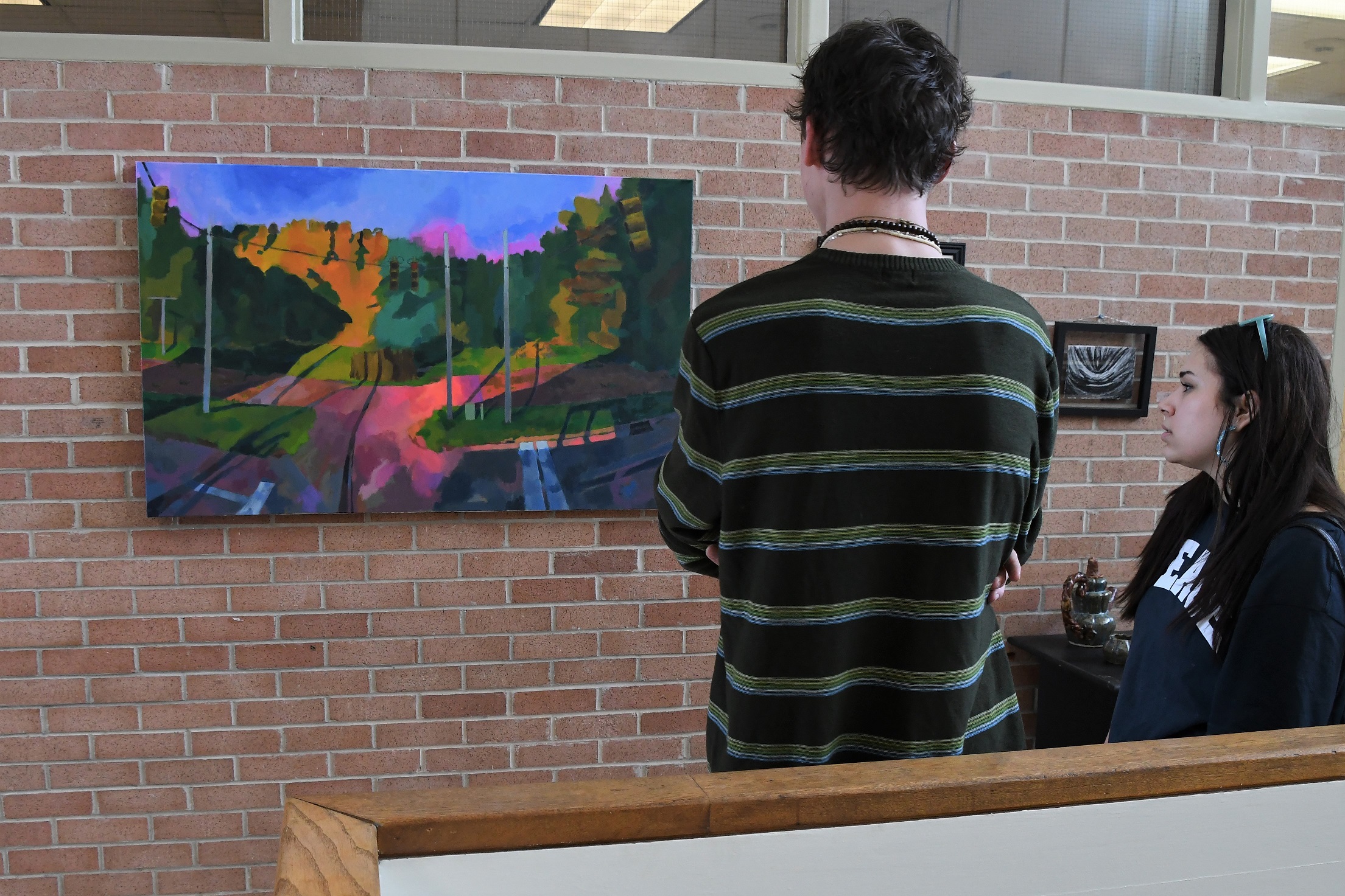 Students look at two pieces of art hanging on the brick wall inside the library.
