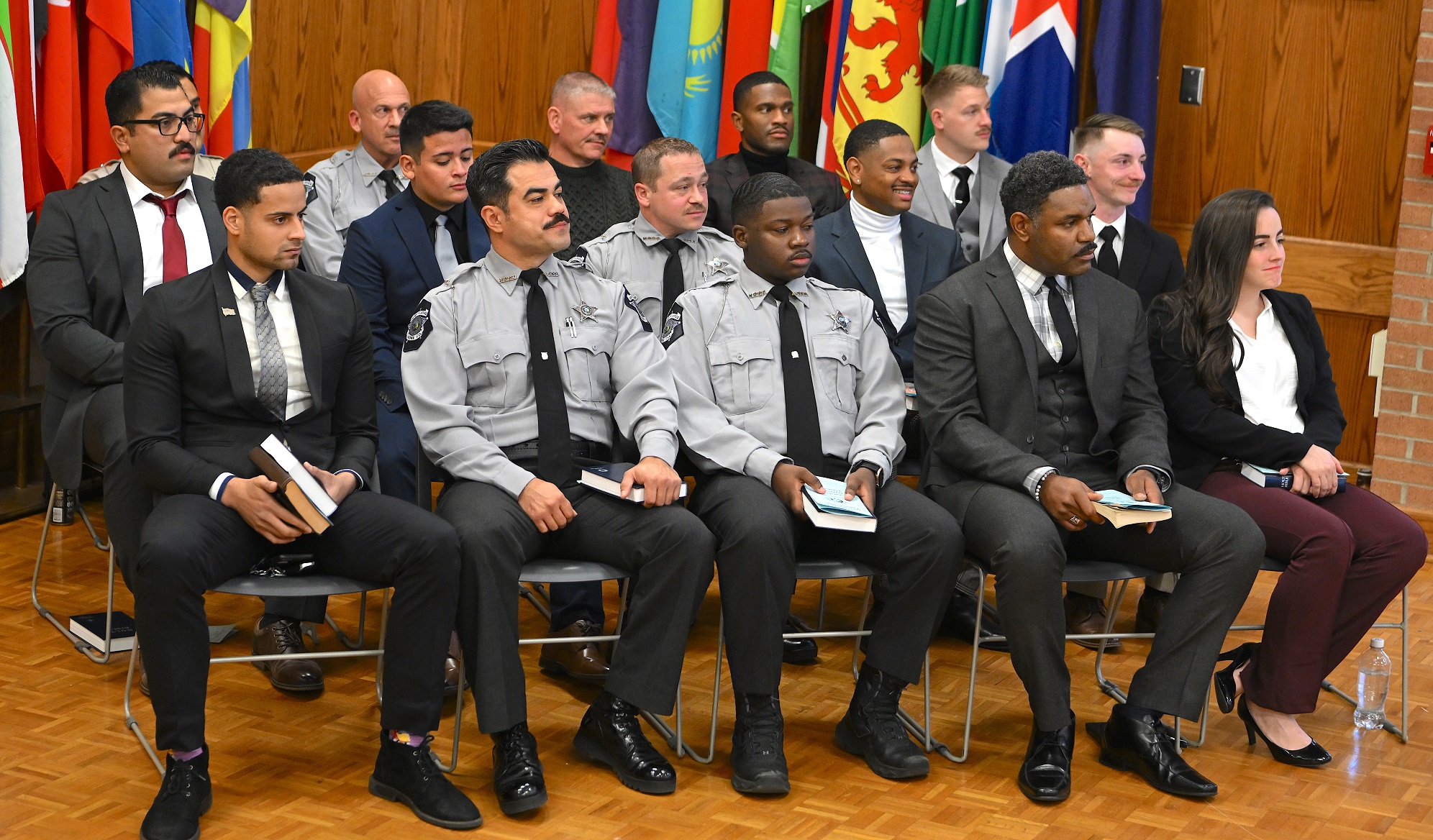 BLET graduates, some dressed in business professional attire and some in law enforcement uniforms, sit in a group at graduation.