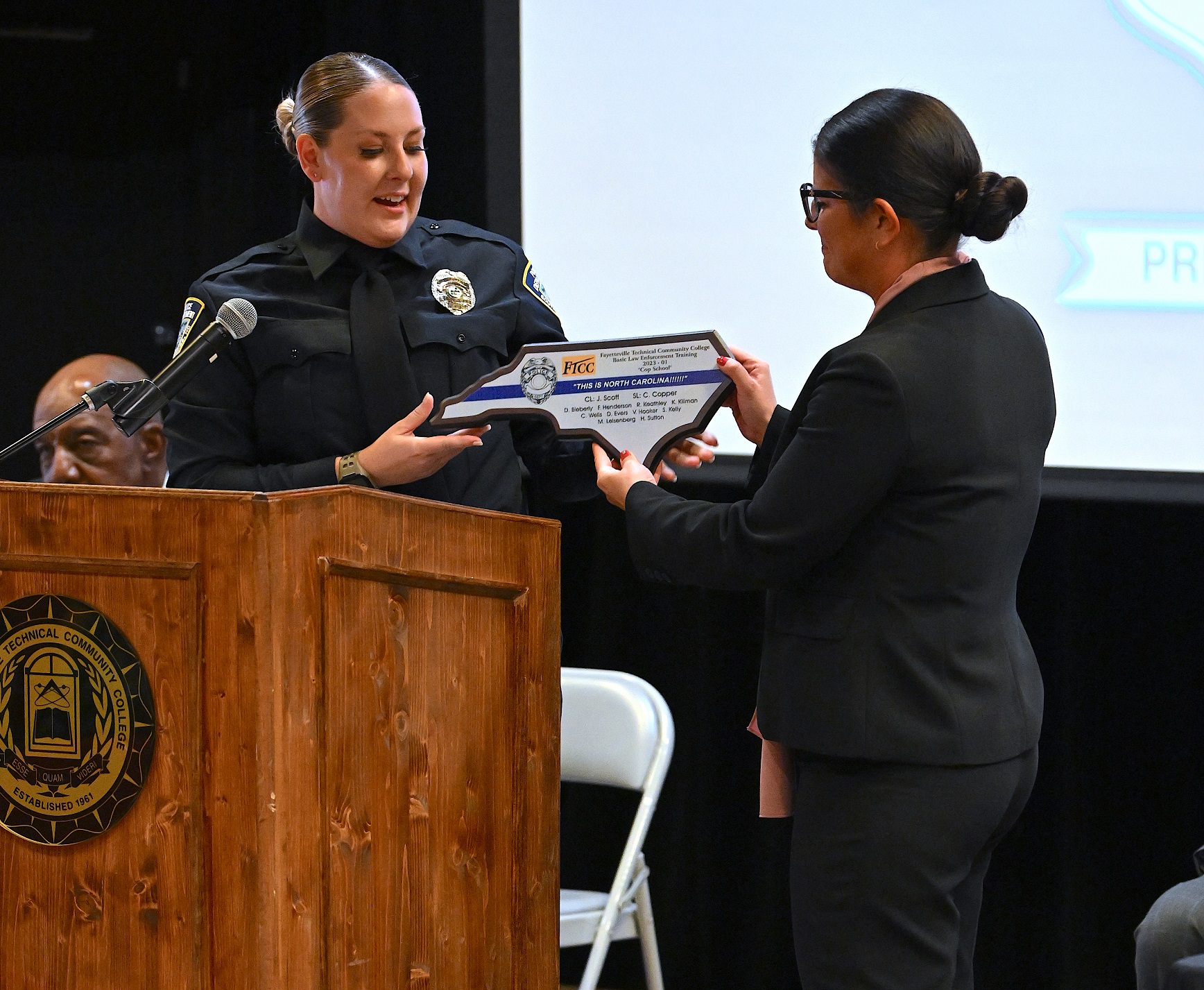 A BLET graduate presents Yovana Vest with a plaque shaped like North Carolina to commemorate the graduating class.