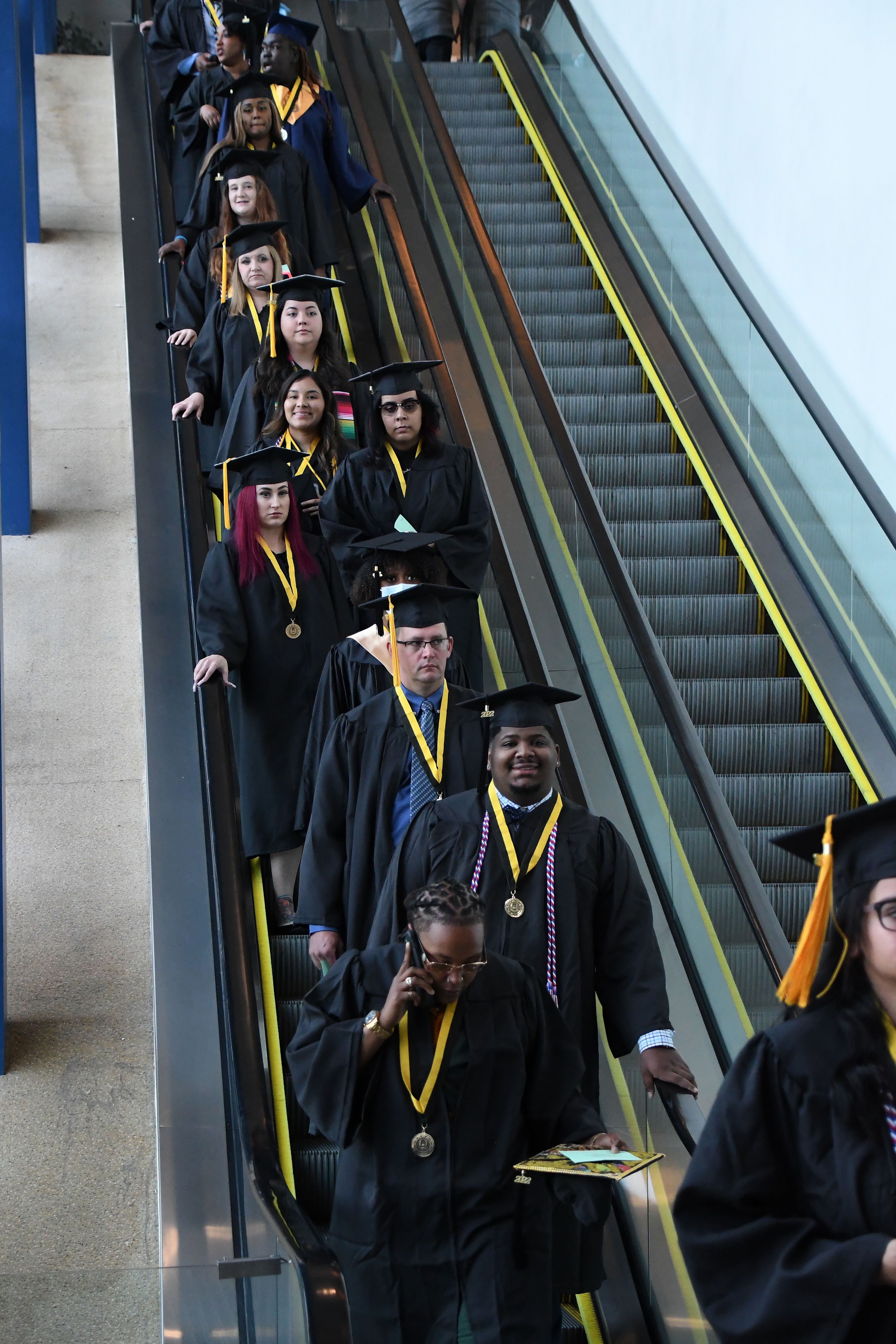 a line of graduates comes down the escalator before the ceremony.