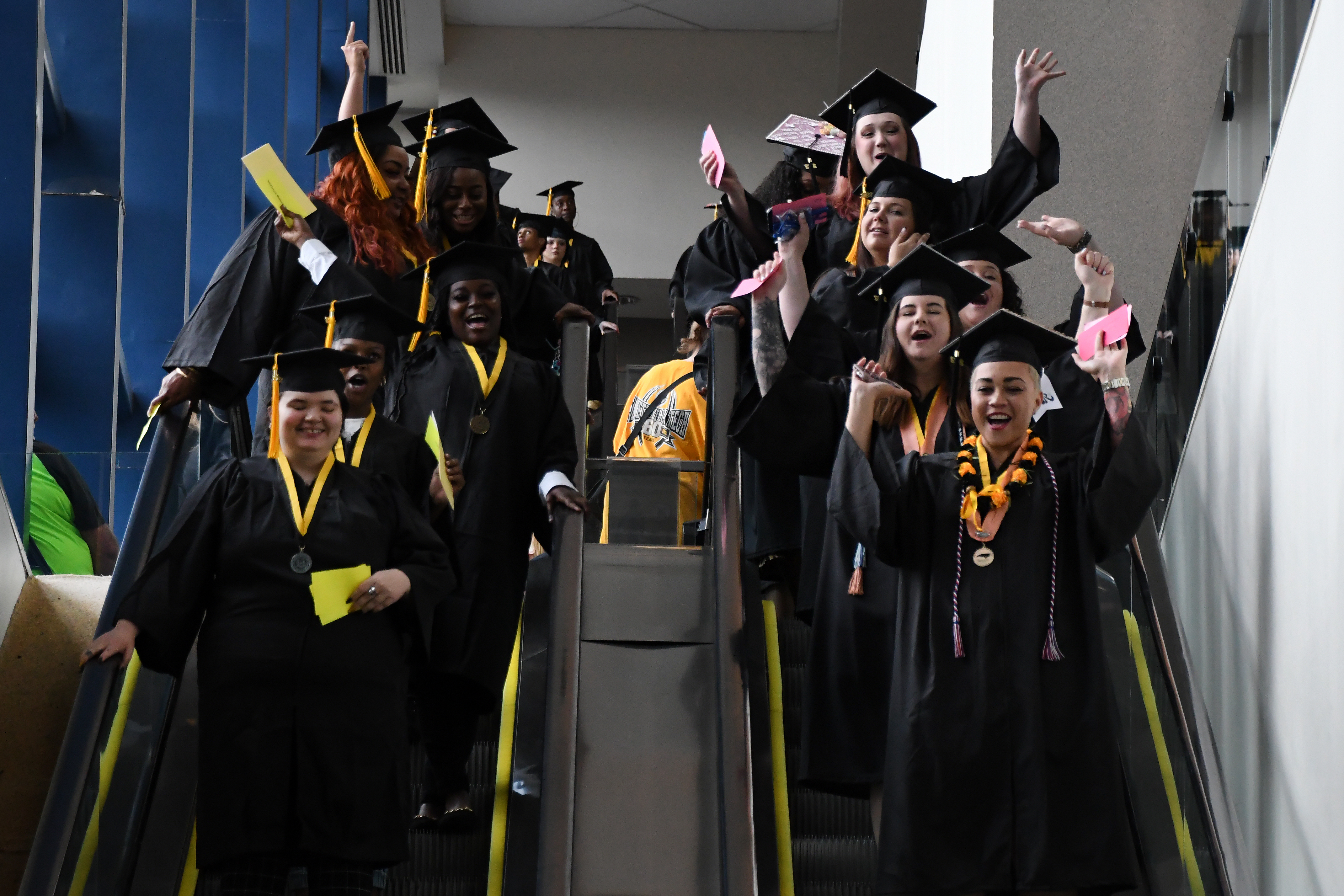 Graduates cheer in celebration as they come down a pair of escalators.
