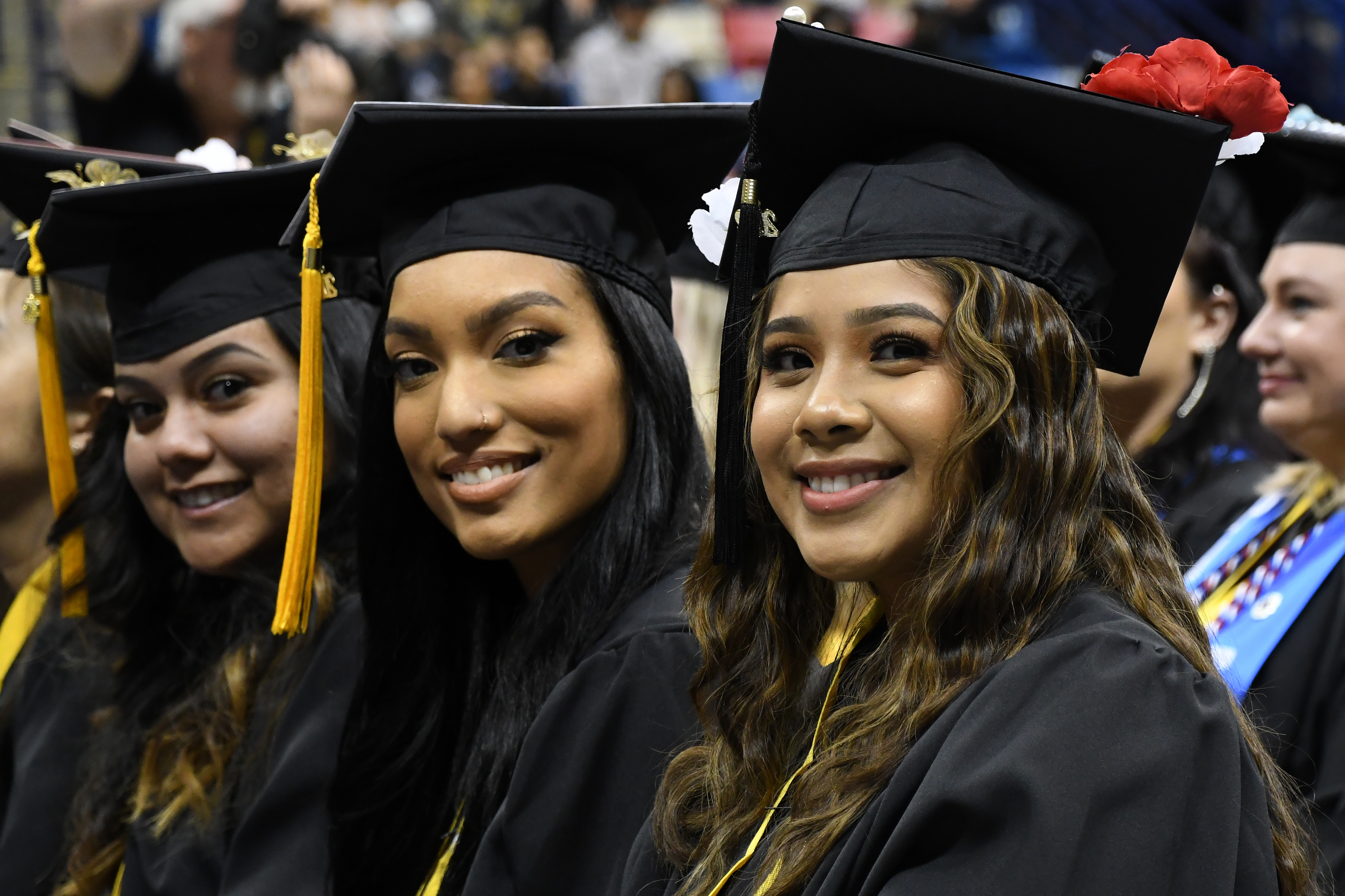 Three graduates sitting in a row smile at the camera.