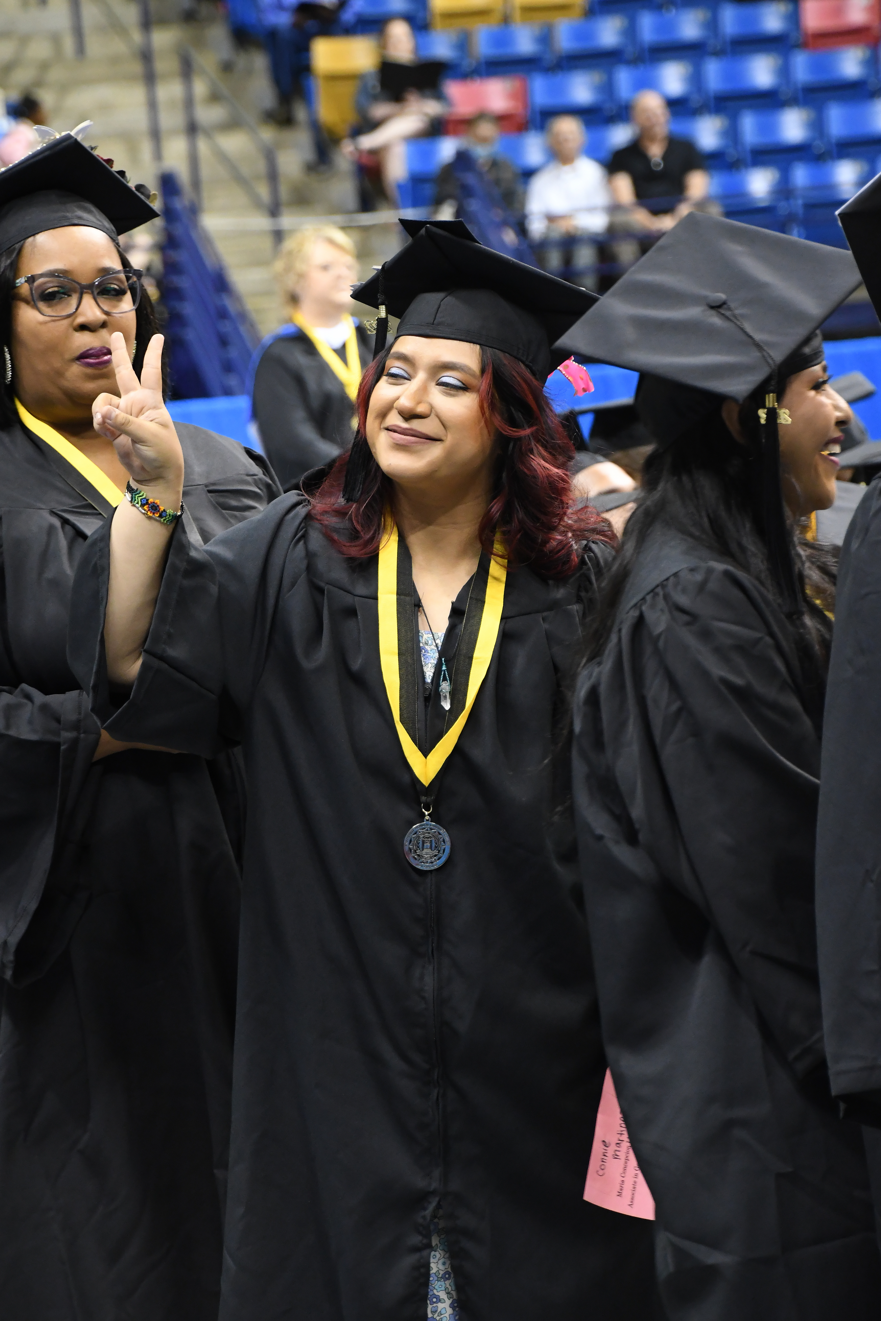 A graduate holds up two fingers in peace sign while looking up into the crowd.