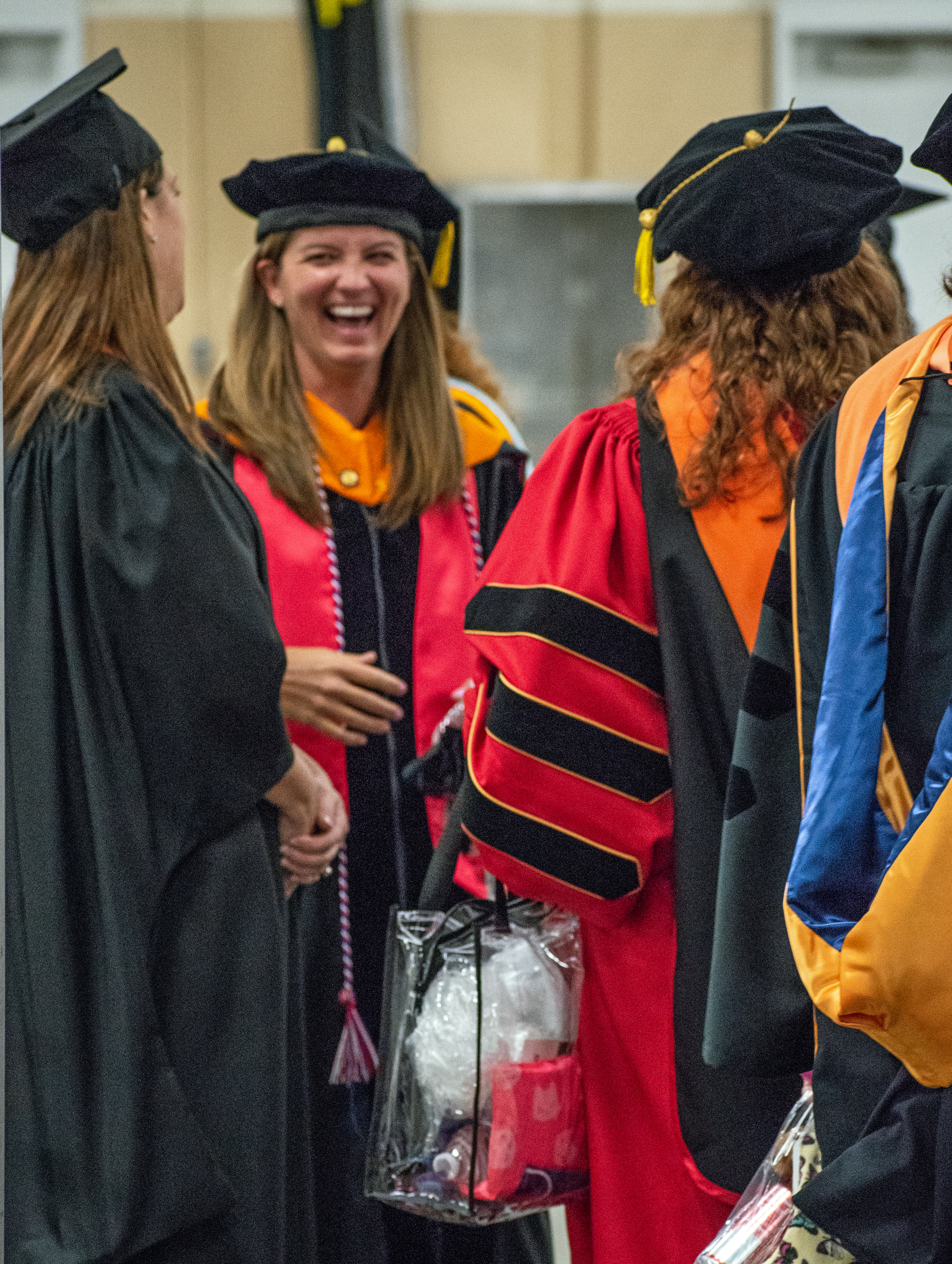 Members of the faculty, dressed in doctoral regalia, share a laugh with a graduate.