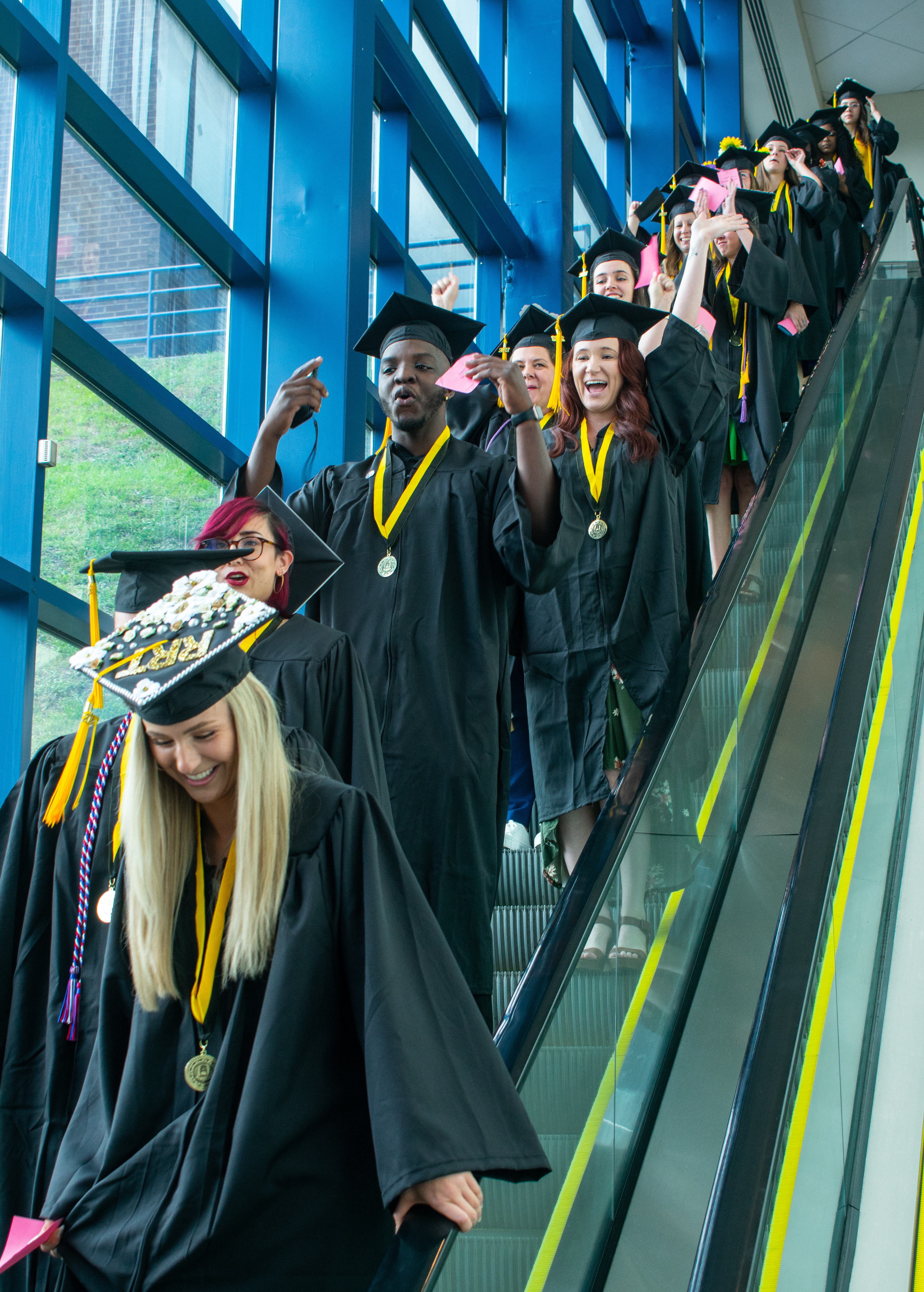 A line of graduates comes down the escalator before graduation.