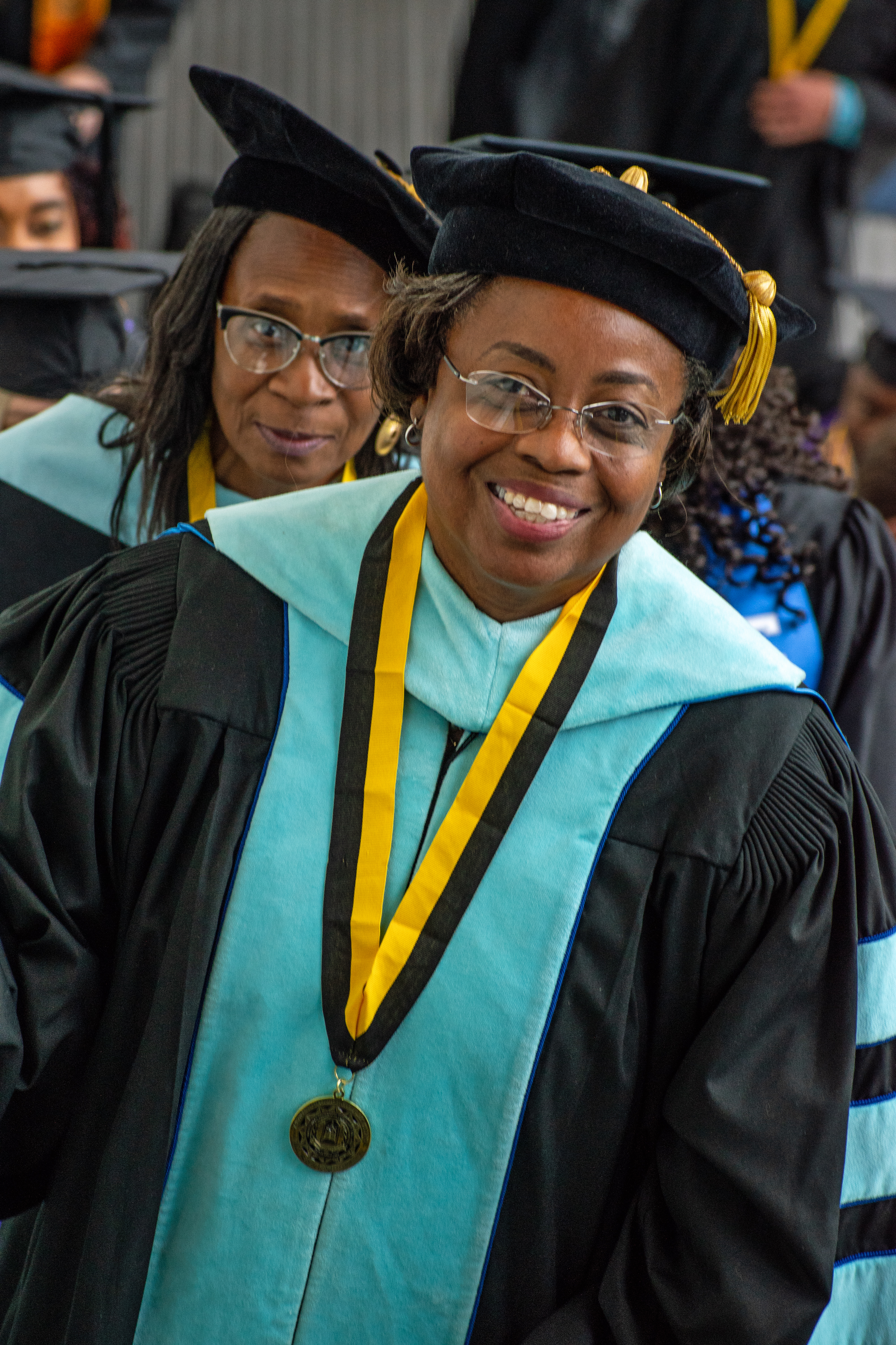 Two women in doctoral regalia with teal trim smile at the camera.