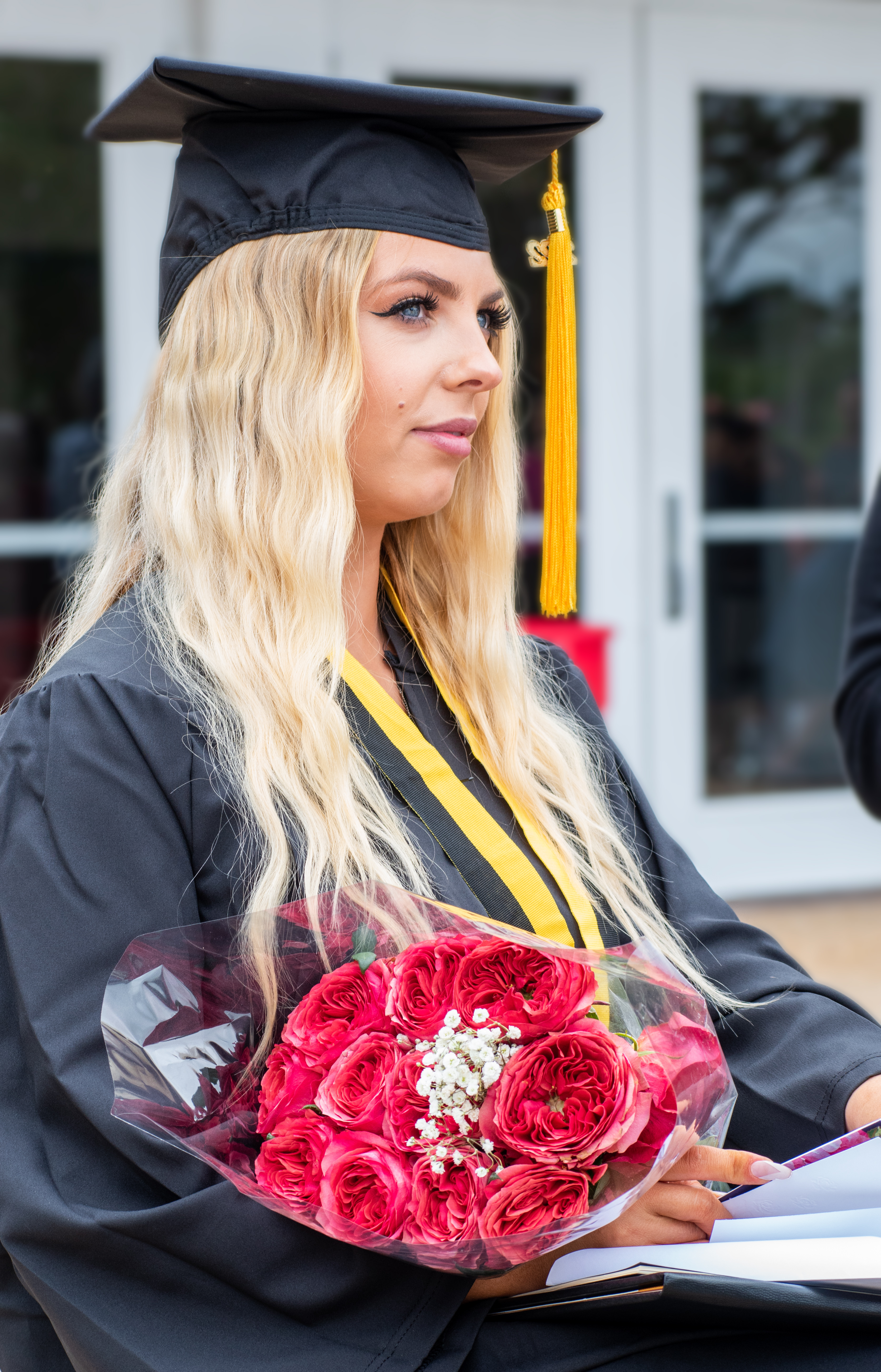 A close-up photo of a graduate looking off into the distance while holding a bouquet of roses.