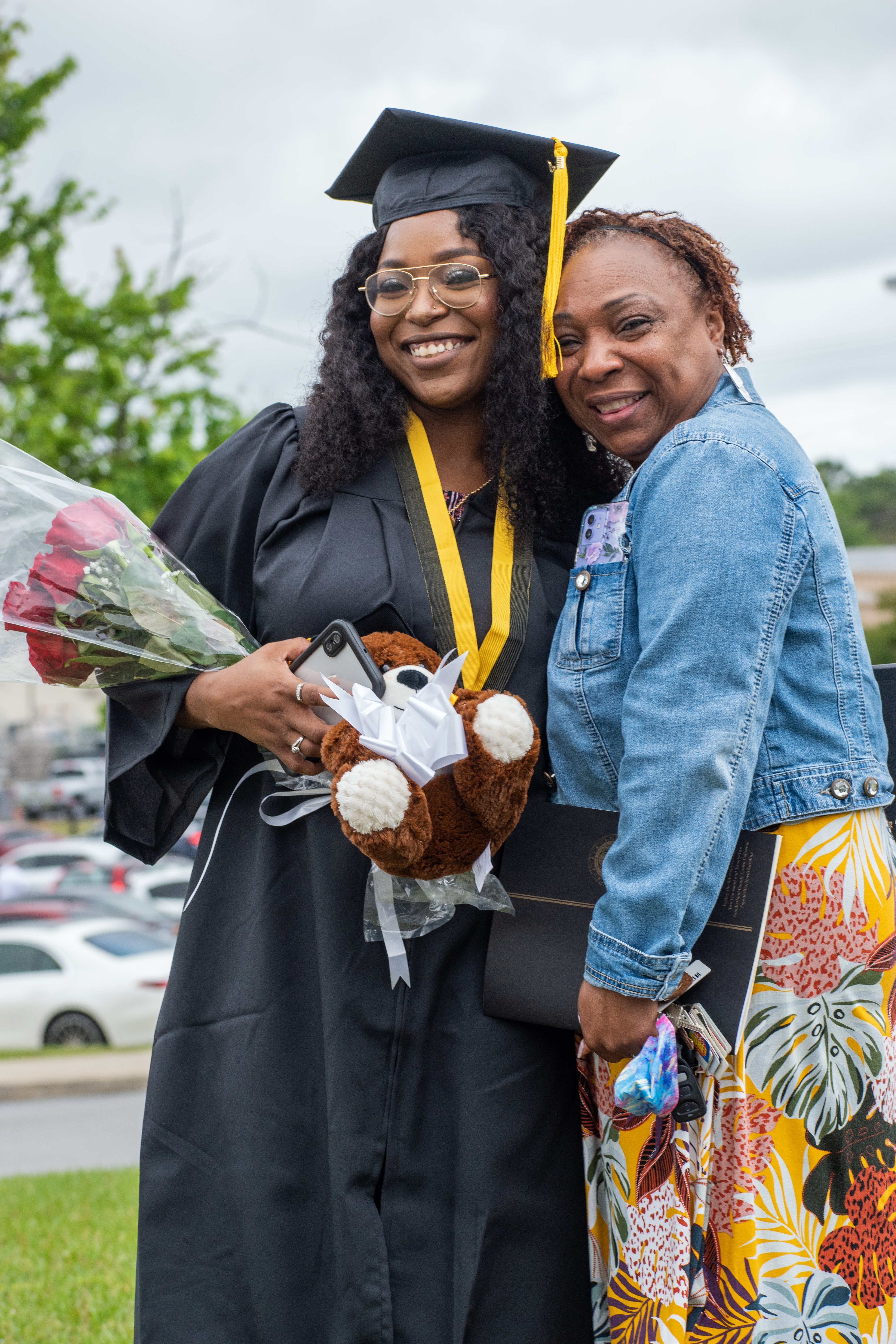 A graduate holding a bouquet of roses and a woman hug and smile for the camera.