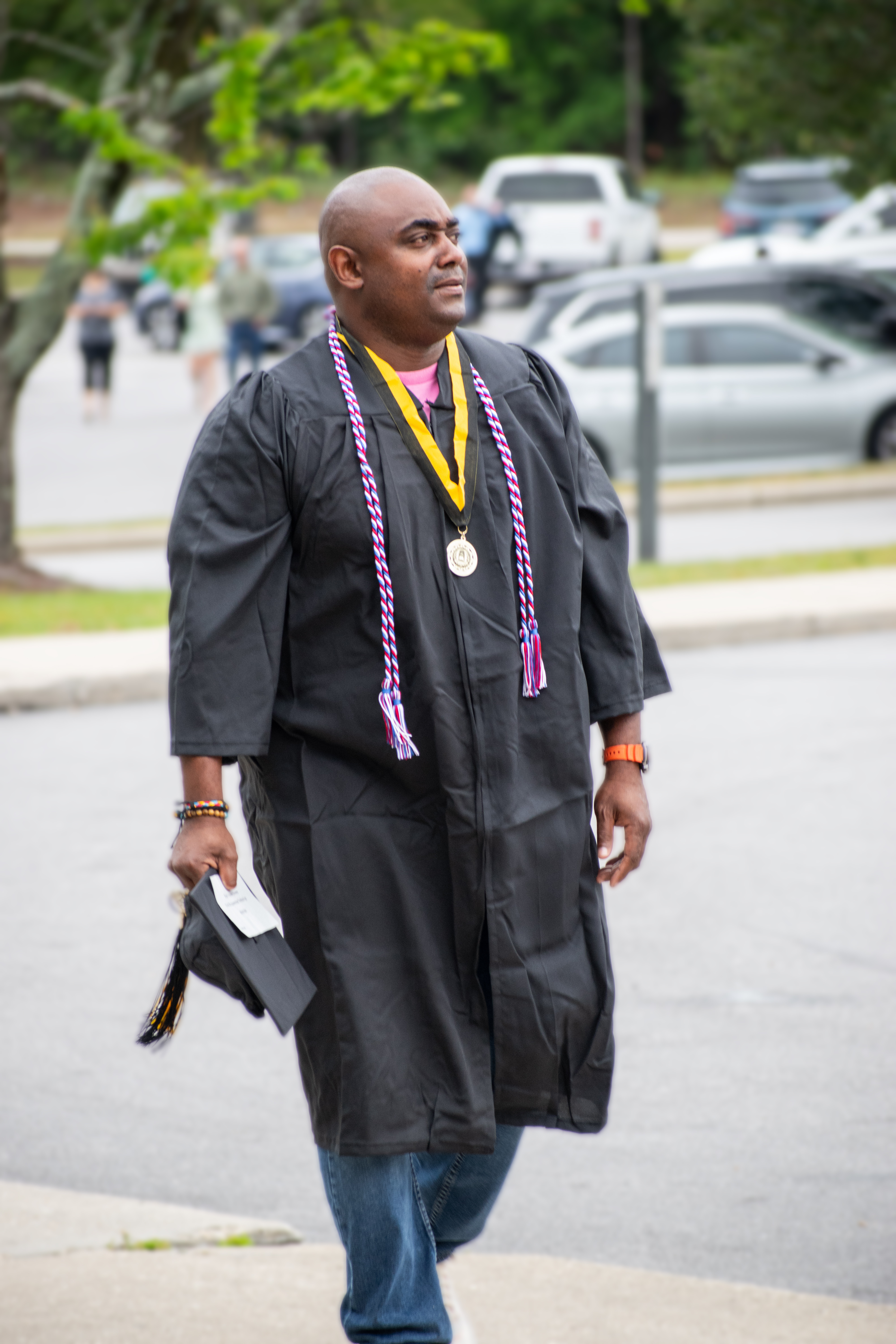A graduate carrying his cap walks up the sidewalk.