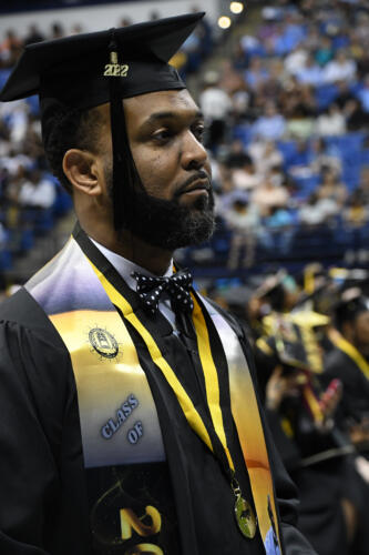 A graduate with a personalize blue and gold stole with Class of 2020 printed on it, looks up at the stage.