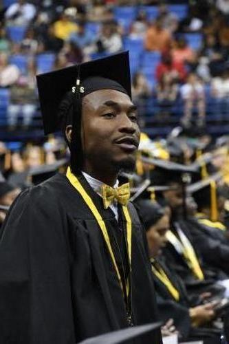 A graduate wearing a gold bow tie with tropical fish on it looks up at the stage.