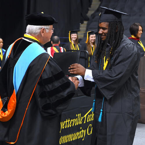 A graduate smiles as he accepts his degree from Dr. Keen while he shakes his hand.