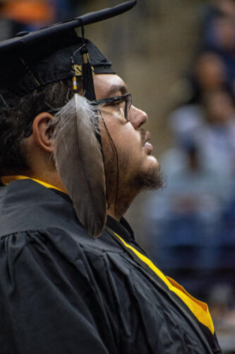 A close-up profile photo of a graduate with a large feather attached to his tassel. 