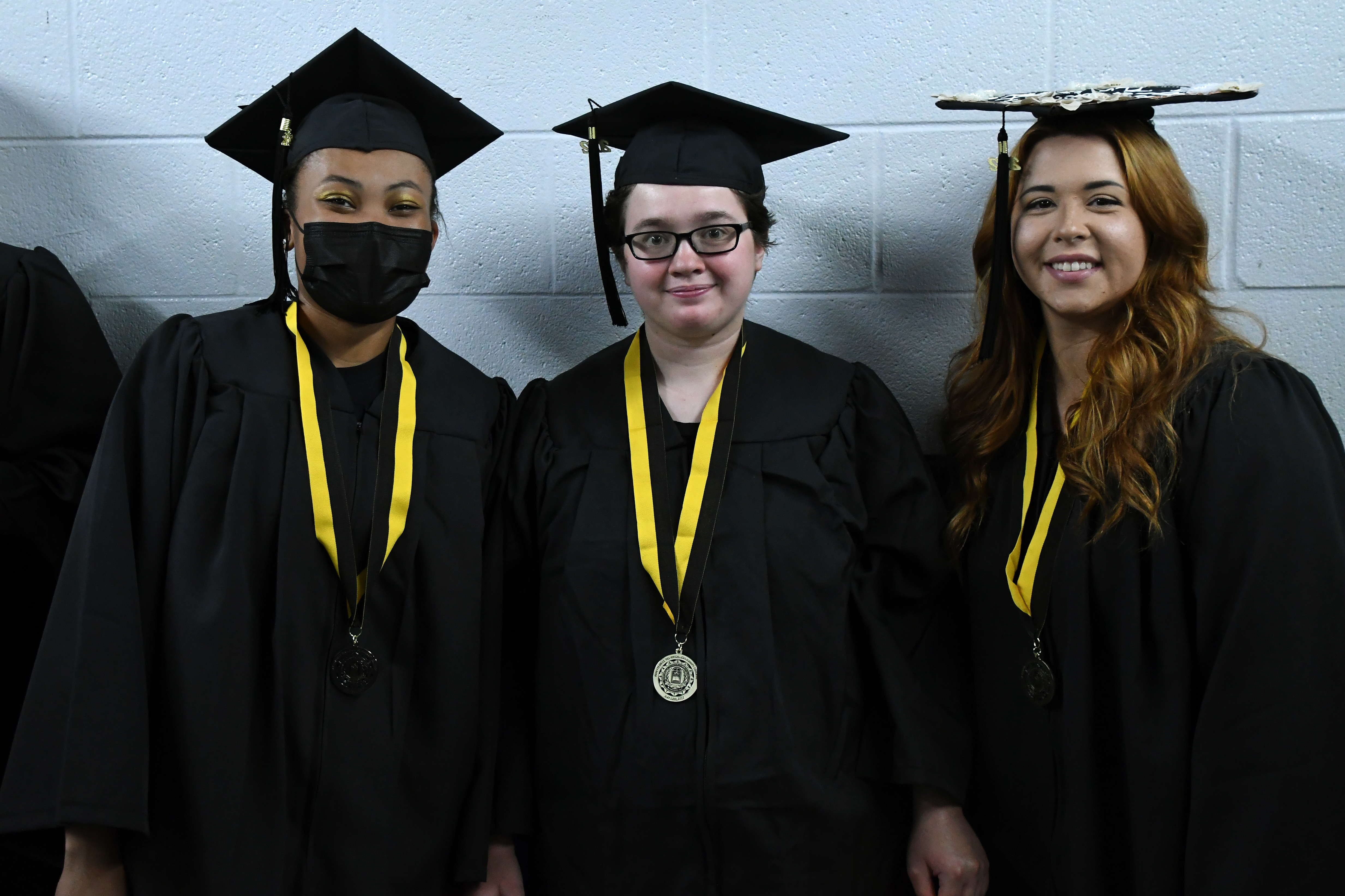 A group of three graduates smile for a photograph.