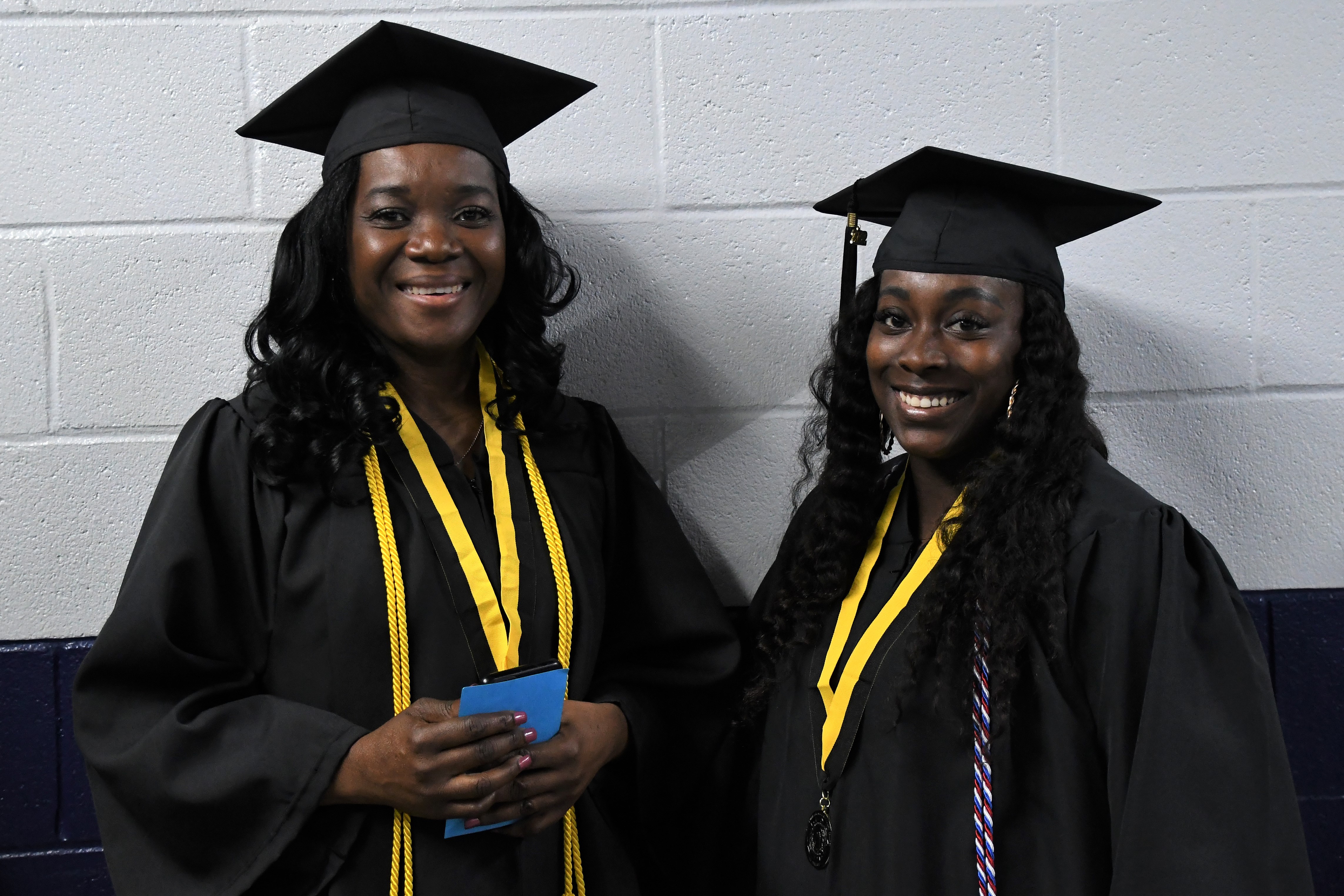 Two graduates smile for the camera in the hallway before graduation.