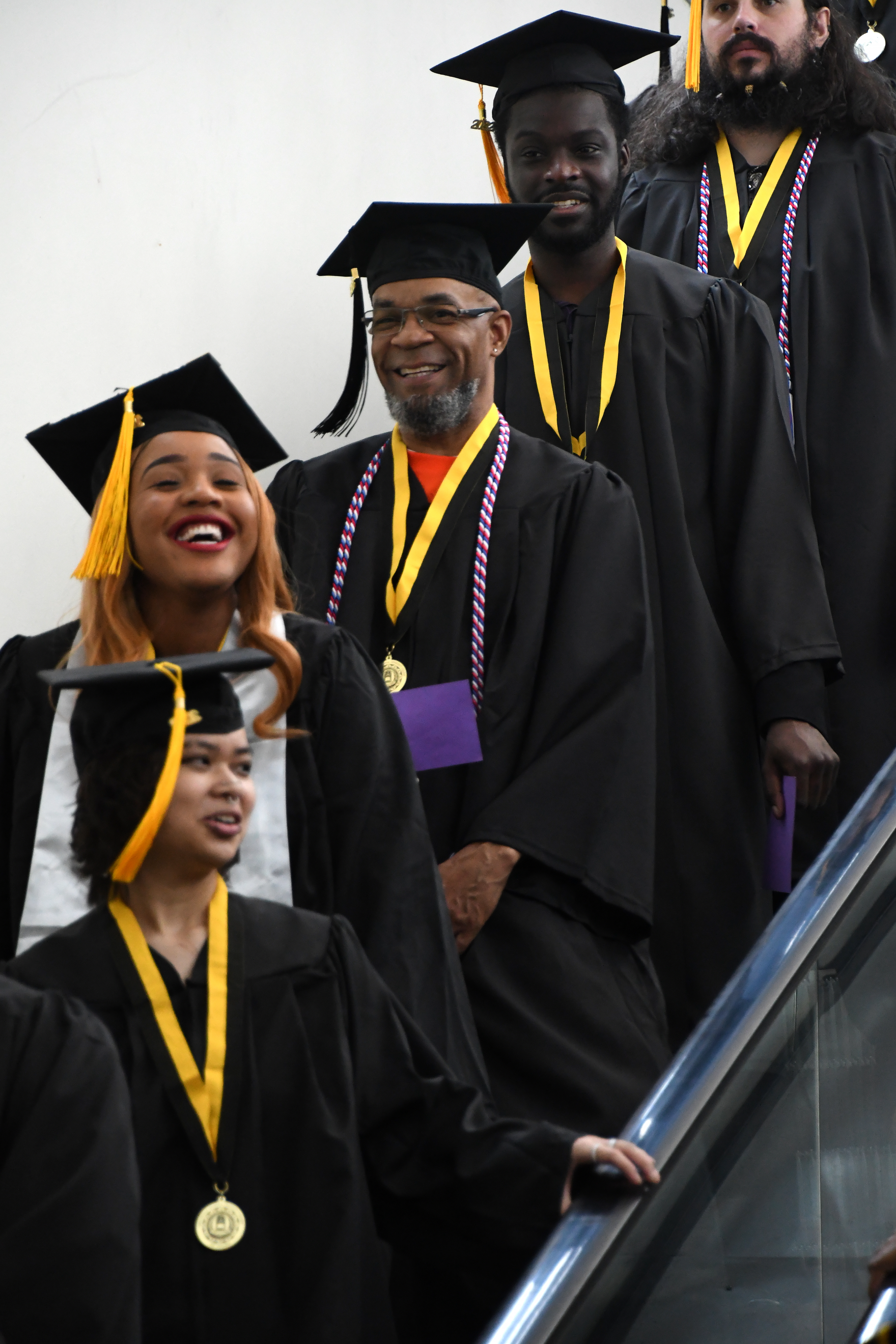 Graduates laugh and smile as they go down the escalator.