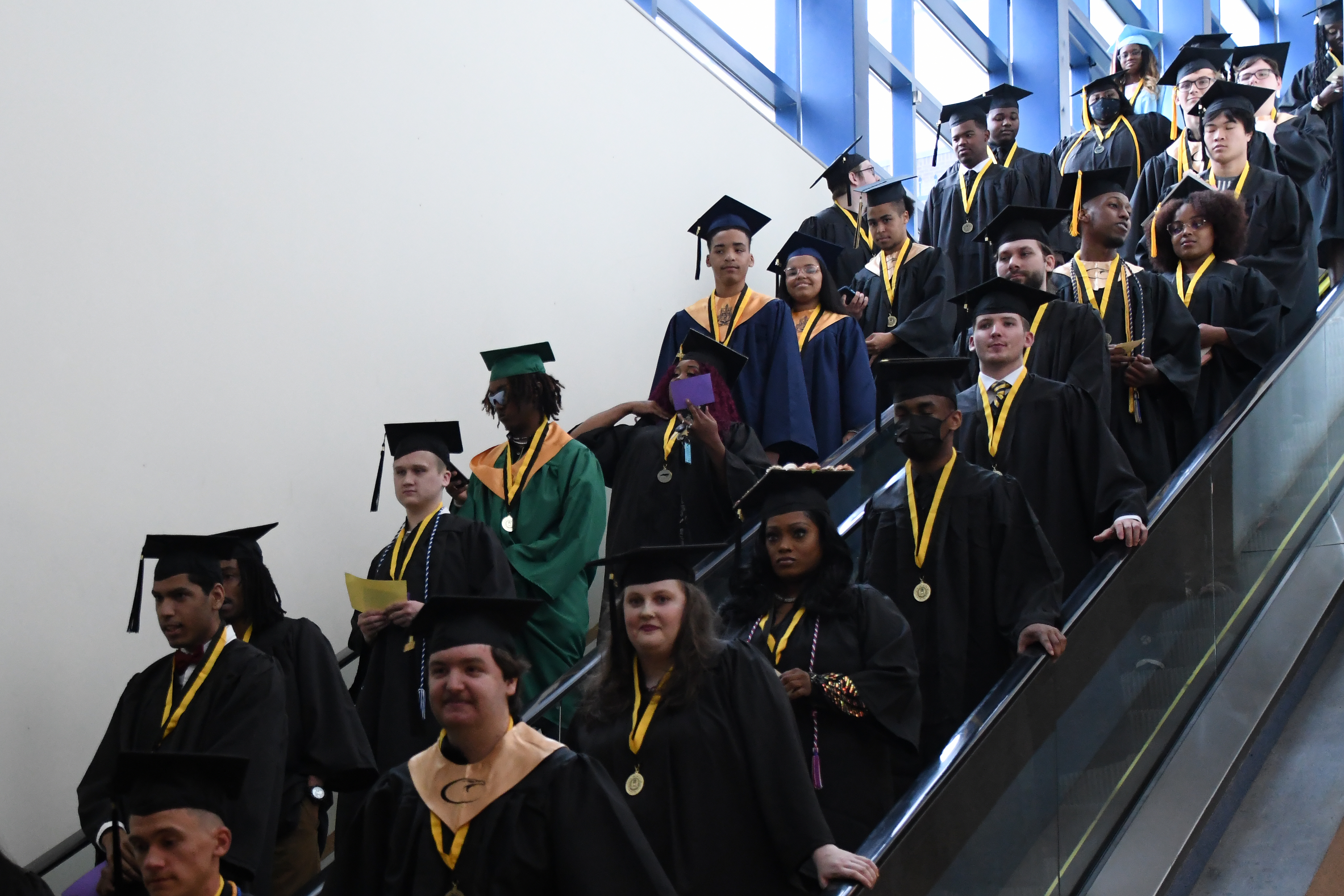 A group of students descends two escalators on their way to graduation.