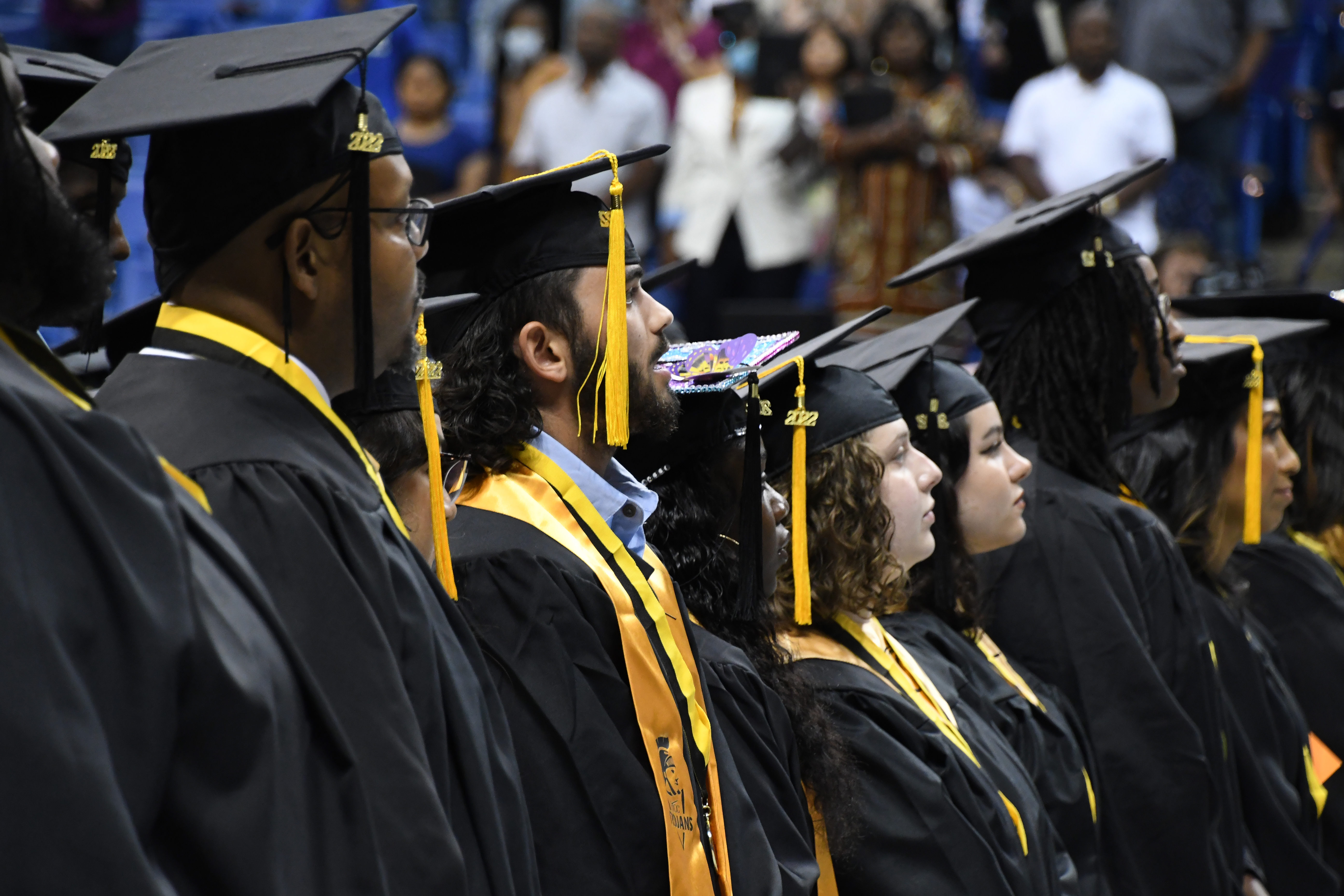 A group of seated graduates looks up at the stage and away from the camera.