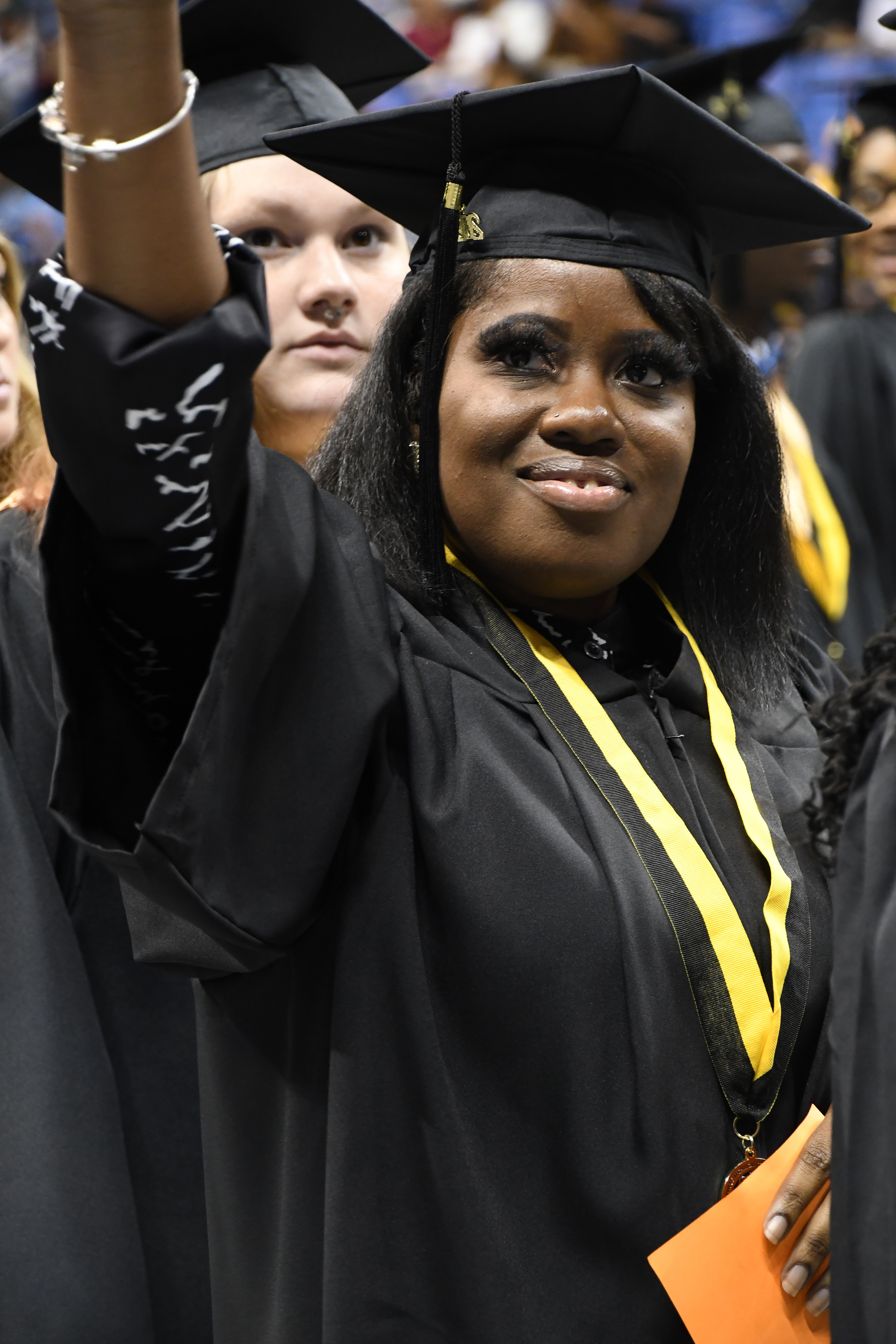 A close-up photo of a graduate smiling and raising her arm to wave to the crowd.