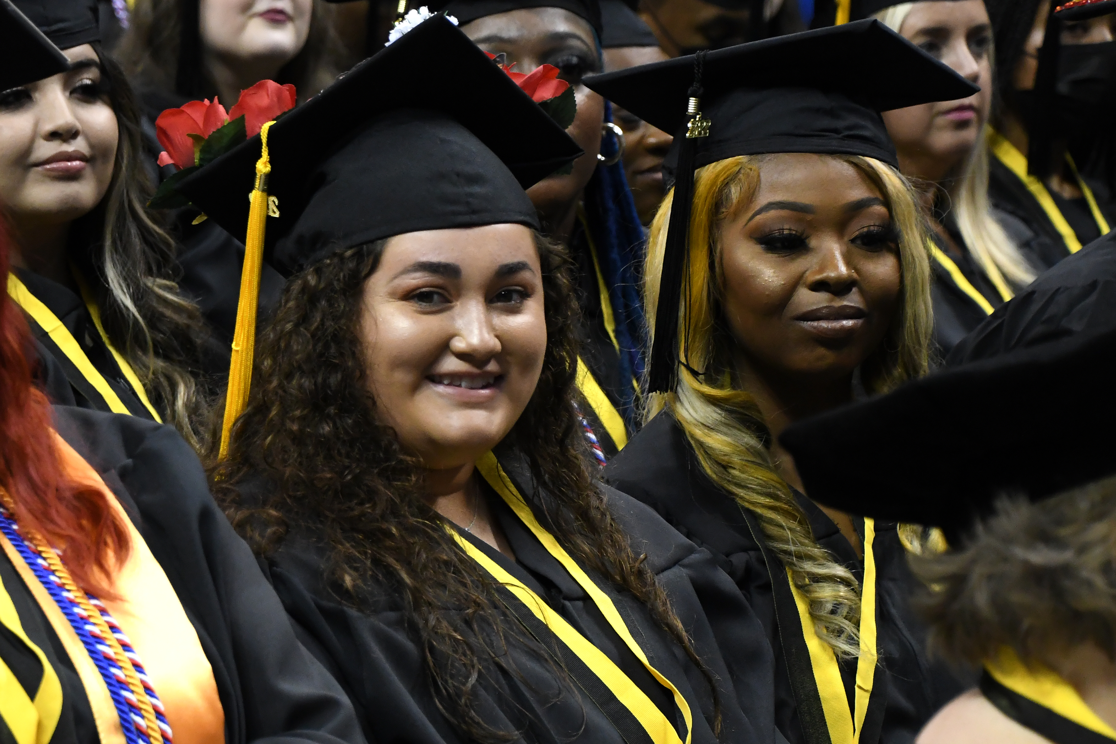 Two seated graduates smile at the camera during graduation.