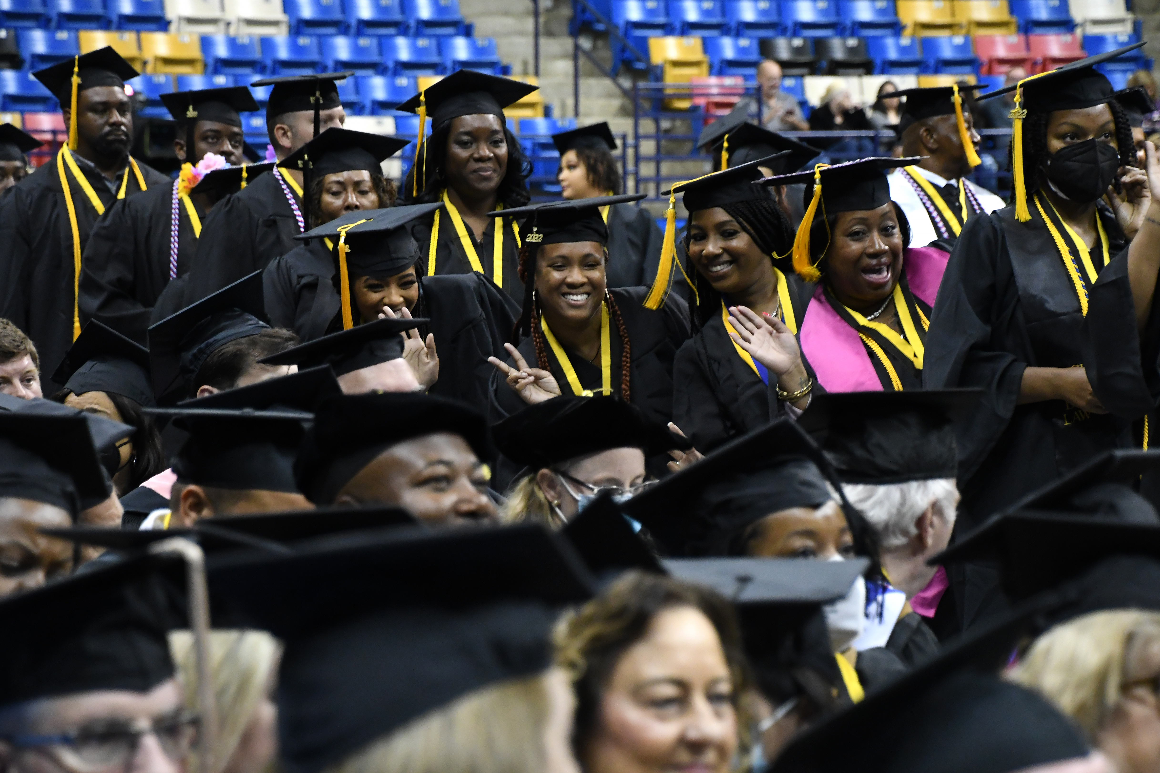 A group of graduates pause to pose for a photo as they walk to their seats during graduation. Seated graduates are visible in the foreground.