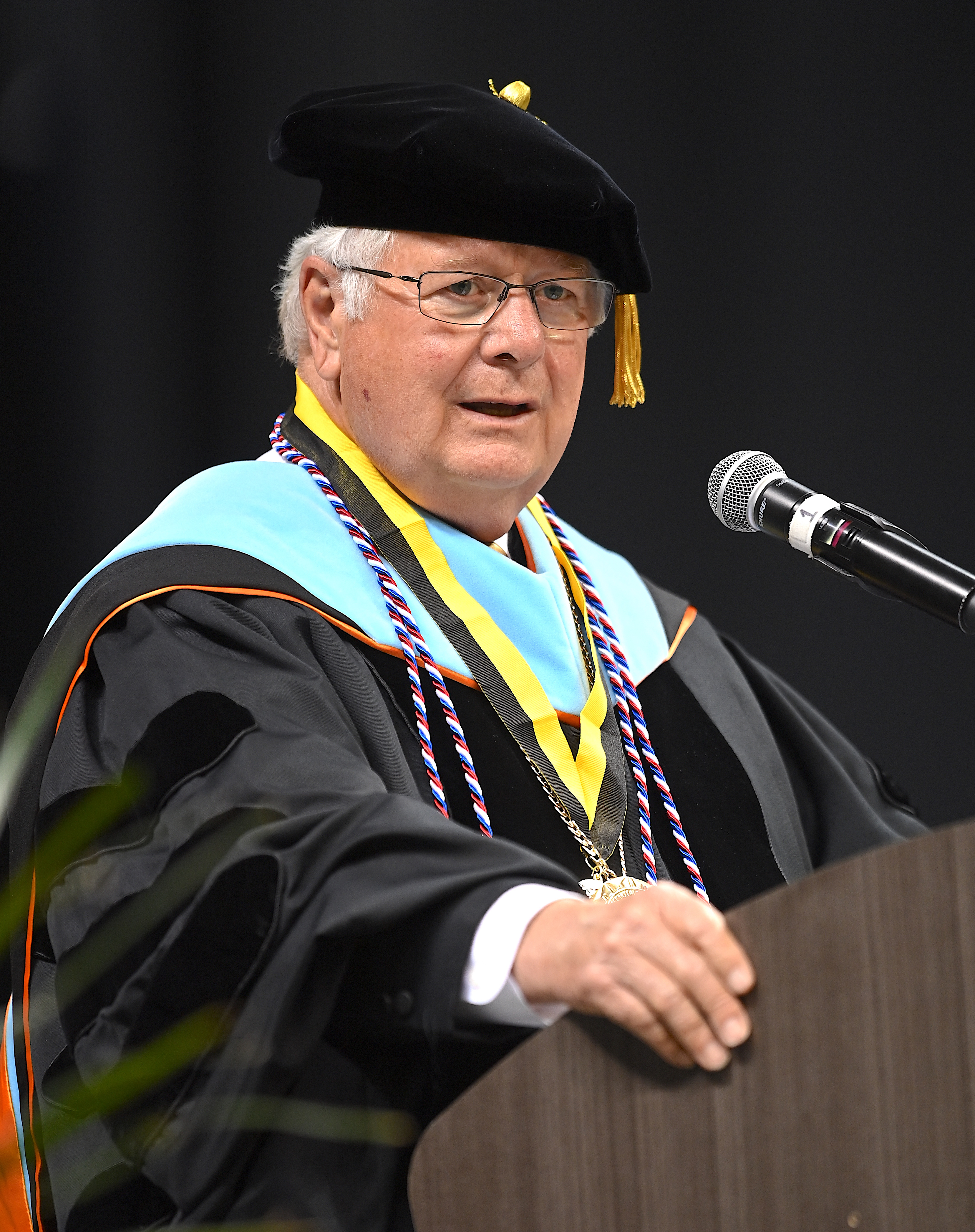 Dr. Larry Keen, dressed in doctoral regalia, speaks at the podium. 