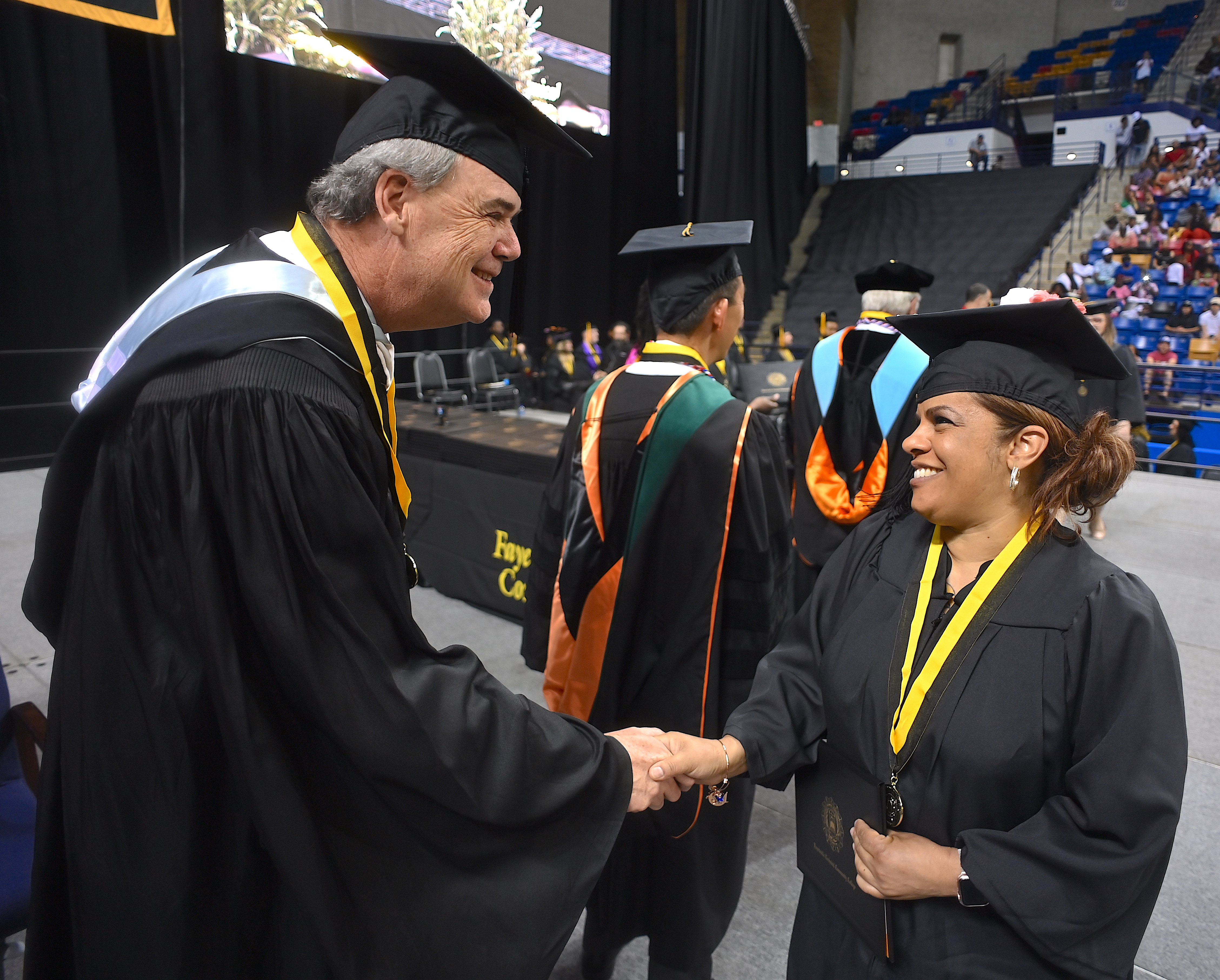 A graduate shakes hands with William Hedgepeth on stage. 