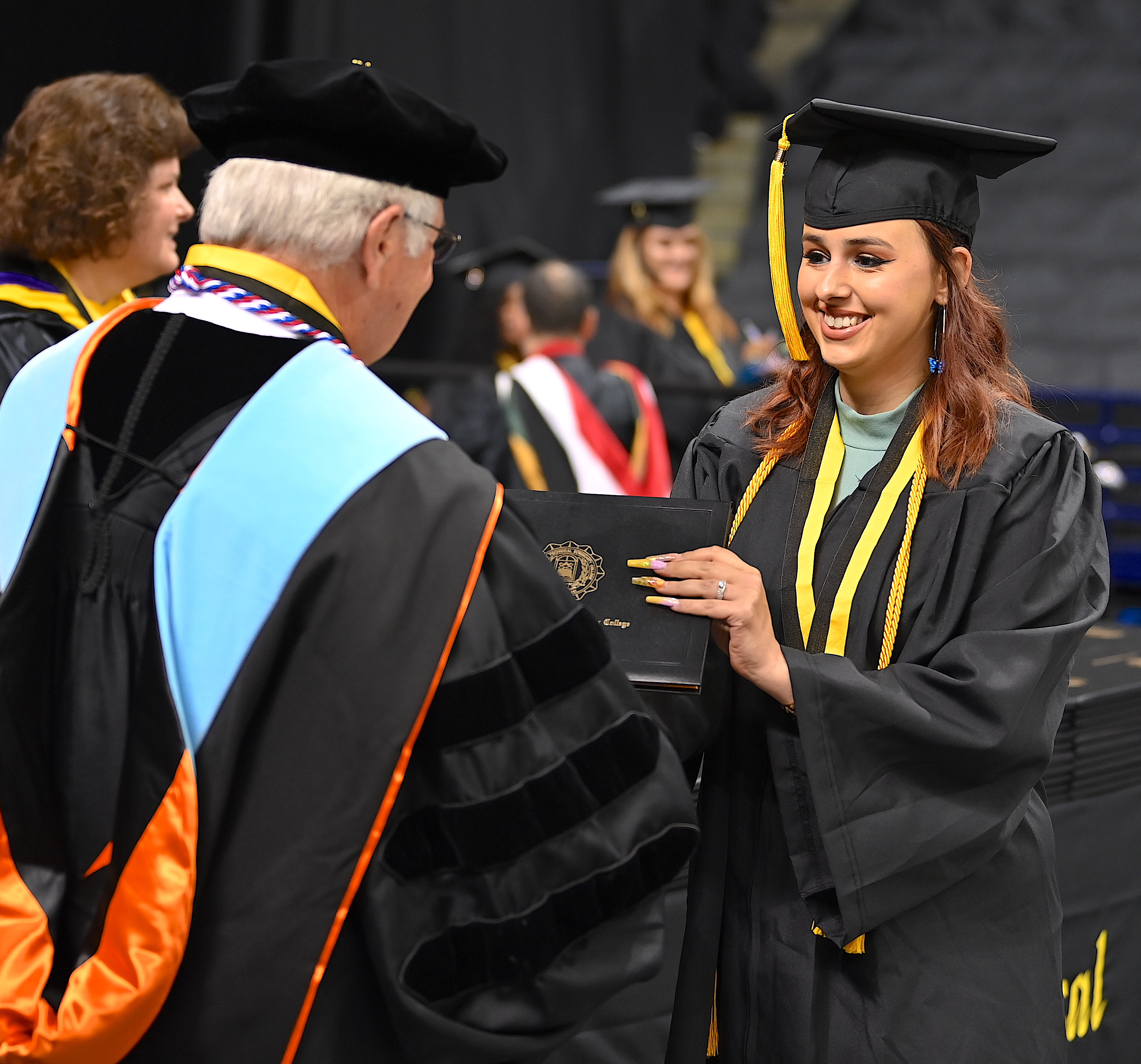 A graduate wearing a gold cord accepts her degree portfolio from Dr. Keen.