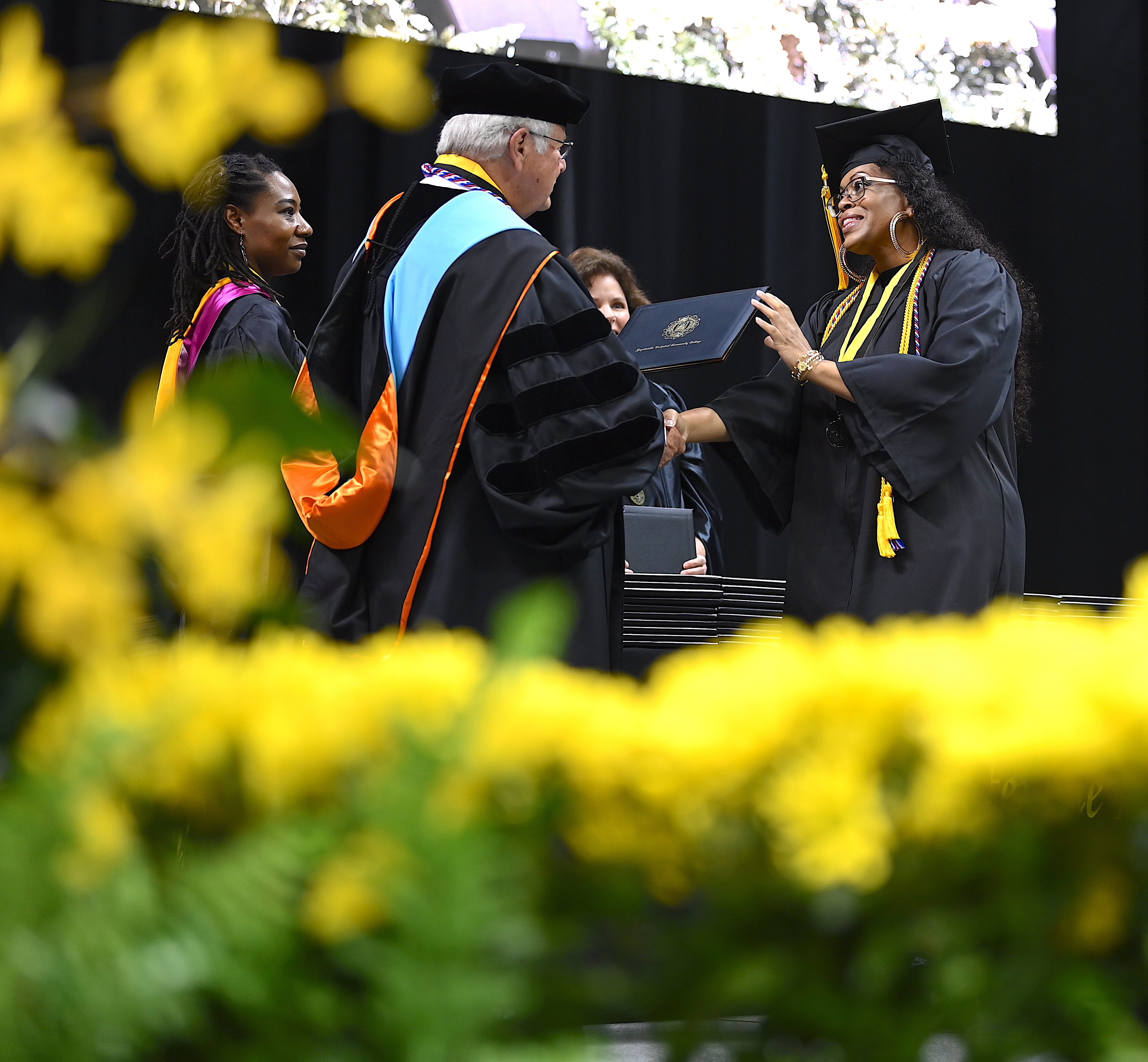 A graduate, wearing glasses and large hoop earrings, accepts her degree portfolio from Dr. Keen.