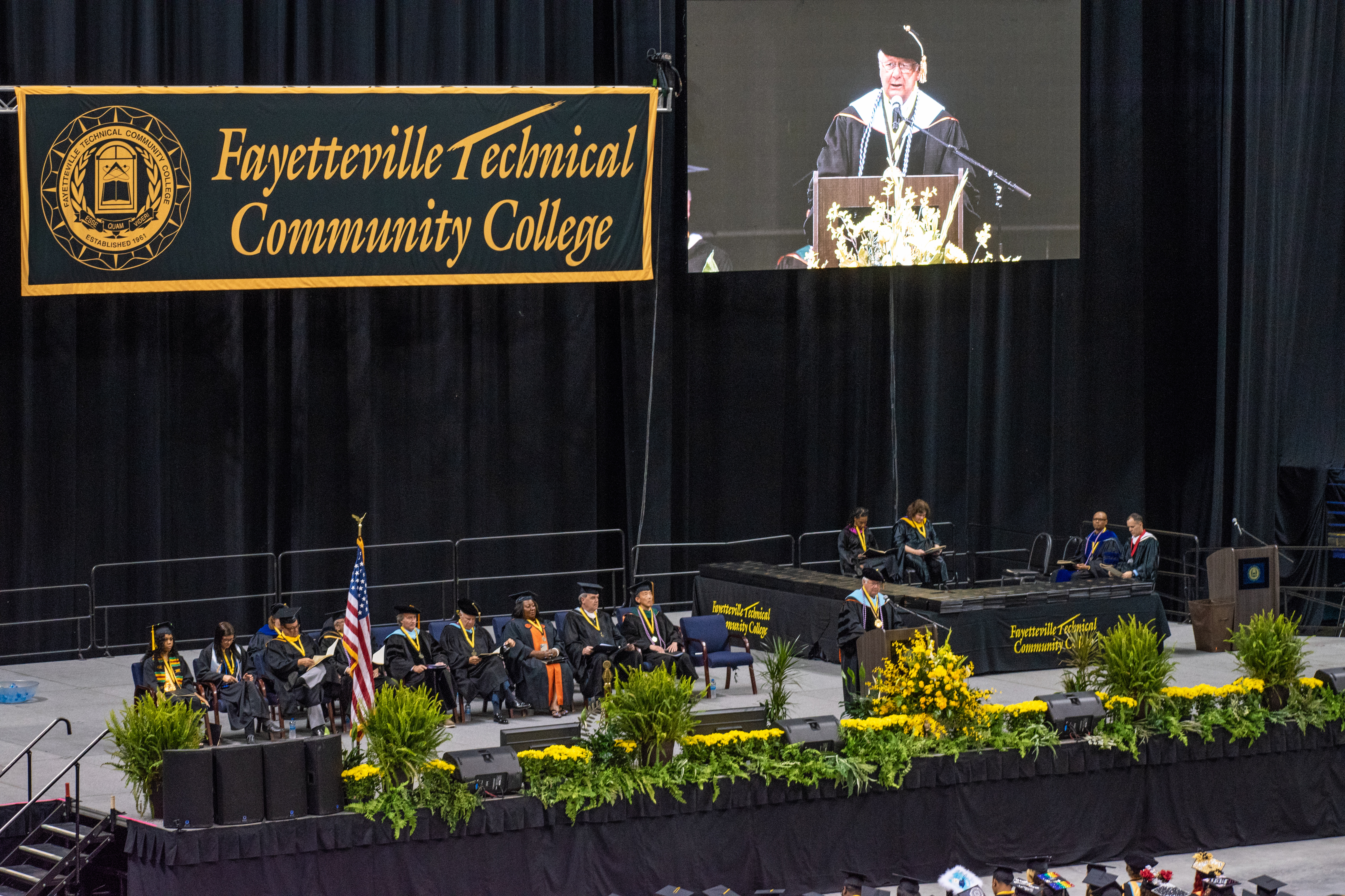 A wide photo looking down on the stage. A Fayetteville Technical Community College banner and a projection screen are visible in the background.