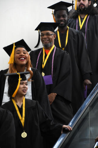 Graduates laugh and smile as they go down the escalator.