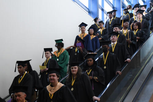 A group of students descends two escalators on their way to graduation.