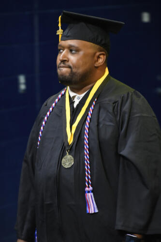 A close-up of a graduate wearing his cap and gown, a medal on a gold and black ribbon and a red, white and blue cord around his neck. 