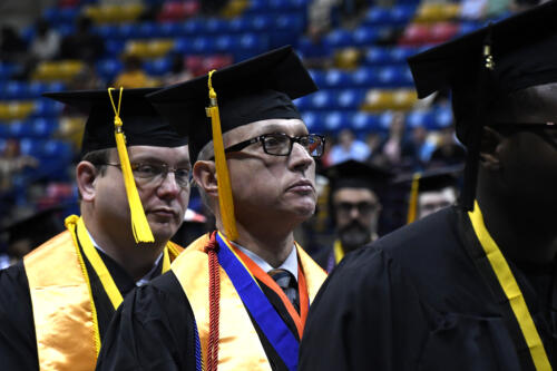 A close-up photo of a graduate wearing a gold stole, a red ribbon, a blue ribbon and a red cord around his neck.