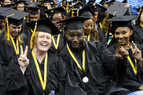 Three graduates pose for the camera. The two on either side are holding up their fingers to make the peace sign.
