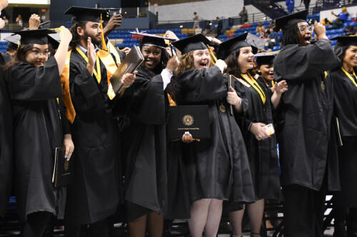 A group of standing graduates celebrate as they turn their tassels at graduation.