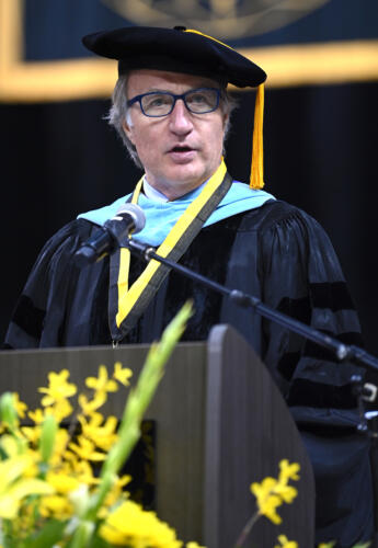 Dr. Mark Sorrells, dressed in doctoral regalia, speaks at the podium.