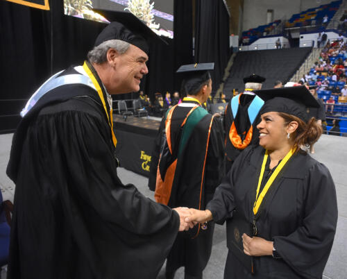A graduate shakes hands with William Hedgepeth on stage. 