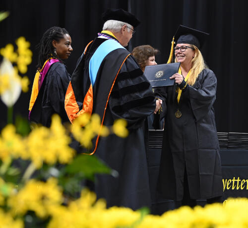 A graduate with long blond hair shakes hands with Dr. Keen as she accepts her degree portfolio.