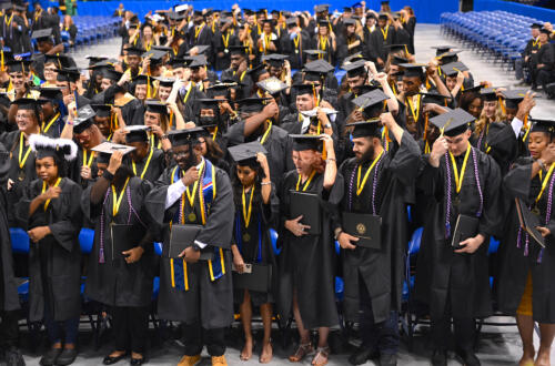 A group of graduates, standing, turn their tassels.