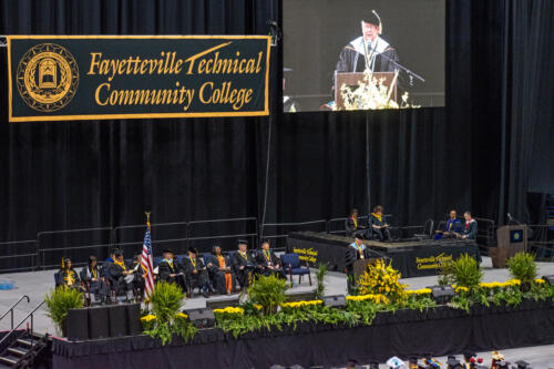 A wide photo looking down on the stage. A Fayetteville Technical Community College banner and a projection screen are visible in the background.