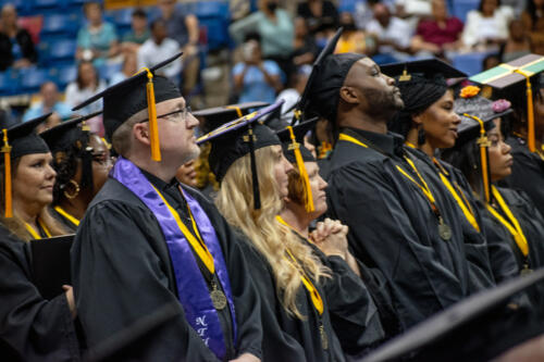 A group of graduates stands looking up at the stage during graduation.